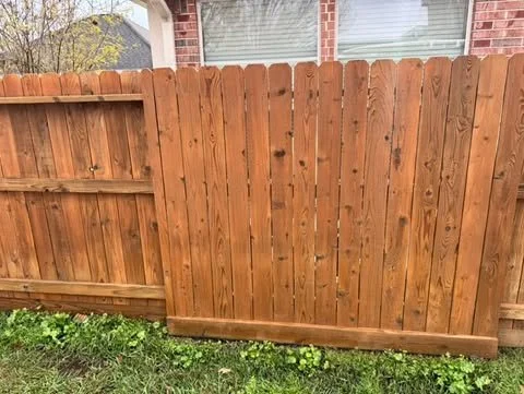 New wooden privacy fence installed in front of a brick house, with a grassy lawn in the foreground.