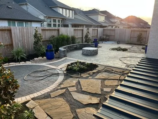 Backyard landscaping with paved stones, plants, and a wooden fence at sunset.