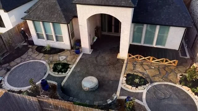 Aerial view of a house front yard with landscaped garden, stone pathways, a circular stone bench, and potted plants.