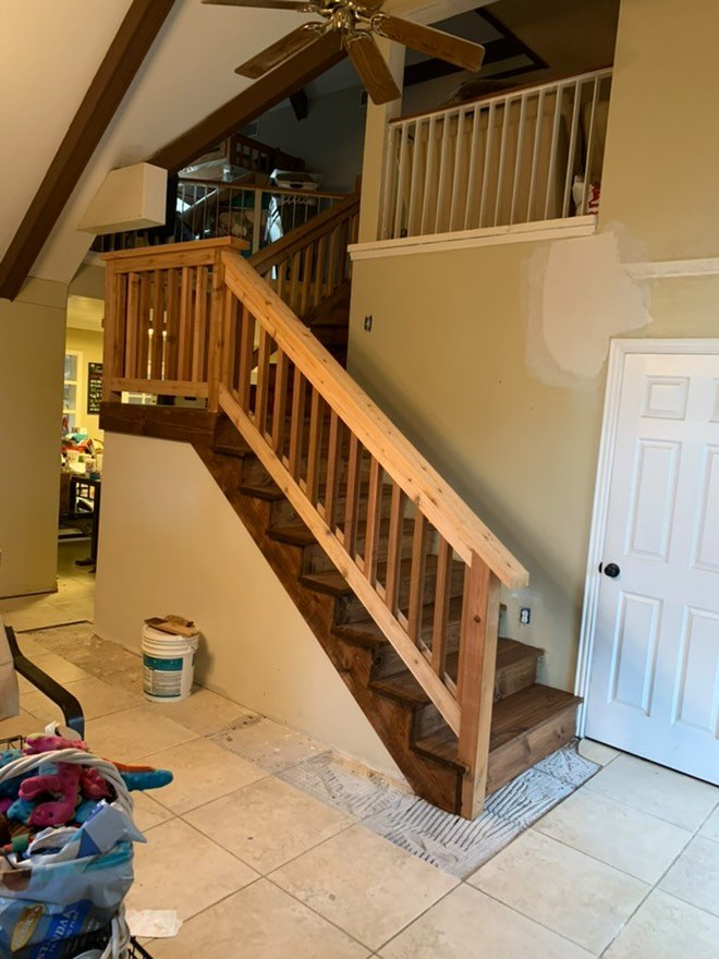 Unfinished wooden staircase leading to an upper floor in a home, with a ceiling fan above and tiled flooring.