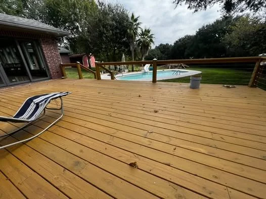 Wooden deck with a lounge chair, overlooking a backyard with a pool, surrounded by trees and a cloudy sky.