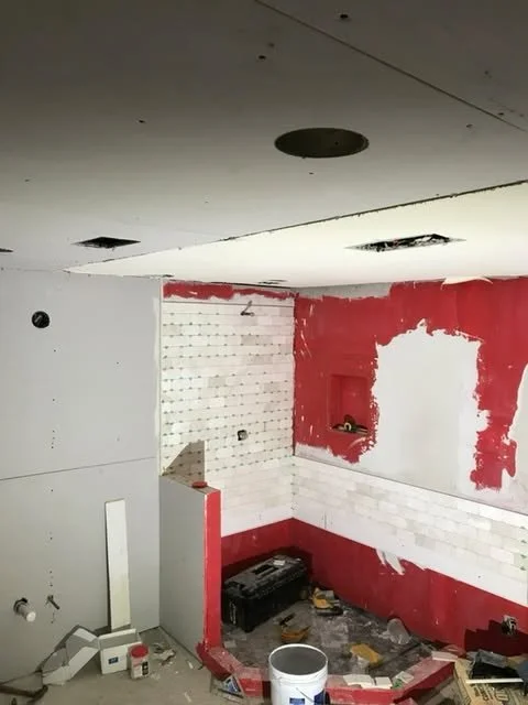 Room under renovation with drywall and exposed wall studs, partially painted red, and construction tools on the floor.