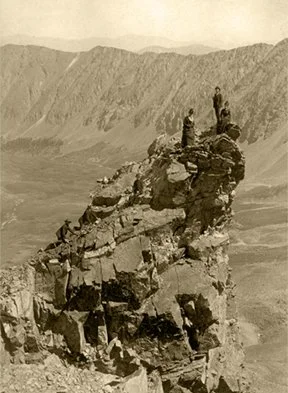 Group of people standing on large rock formation in a mountainous desert landscape