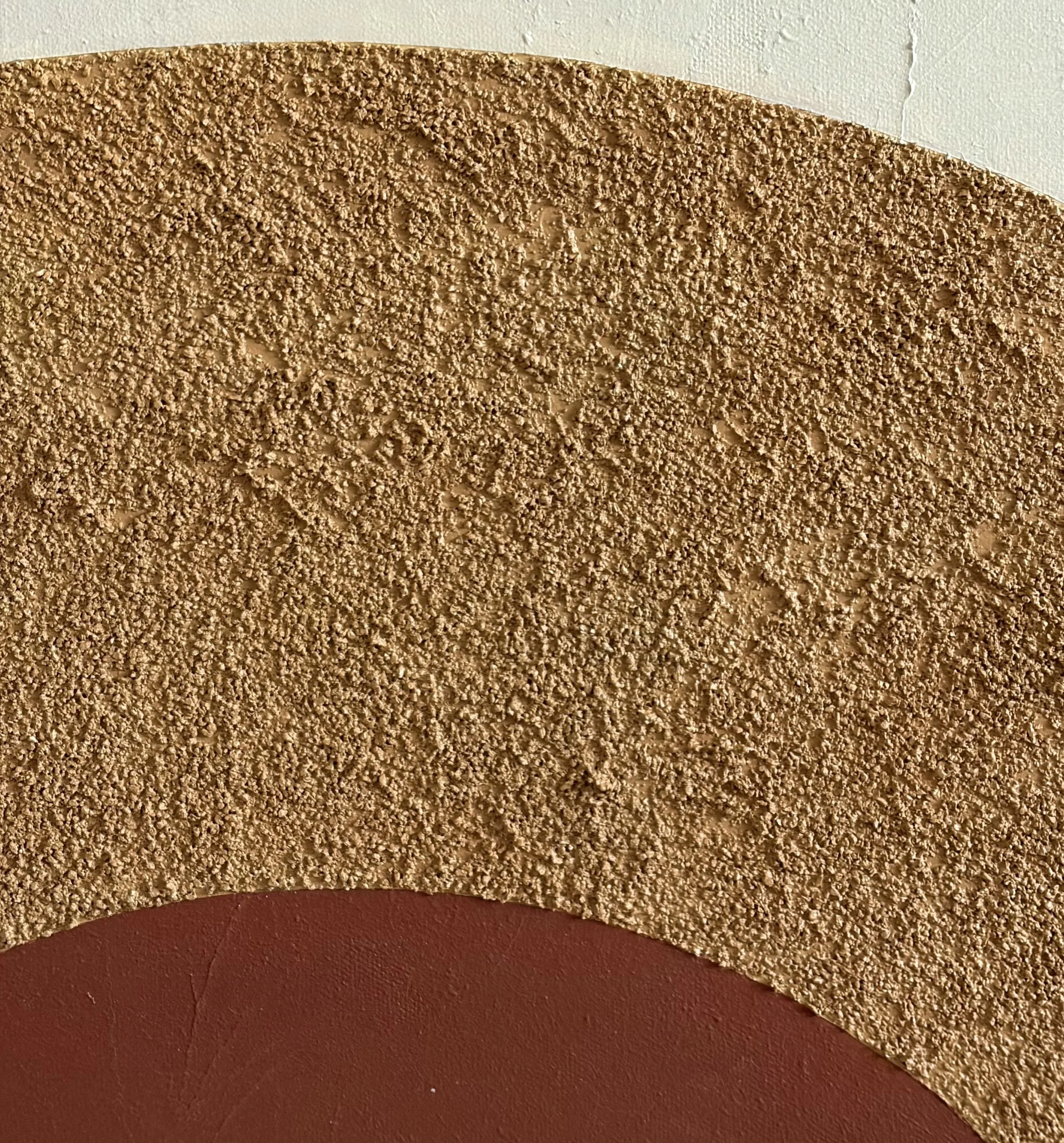 Close-up of a textured brown semicircular wall decoration on a white and reddish-brown wall.