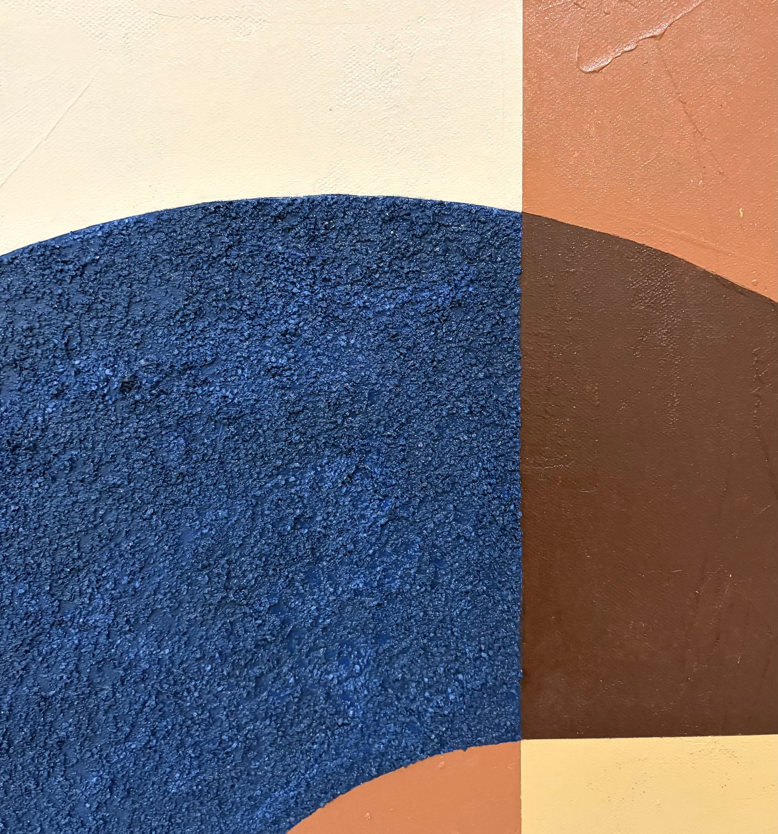 Close-up of textured painted sections in yellow, orange, brown, and blue, with overlapping curved shapes and visible paint texture.