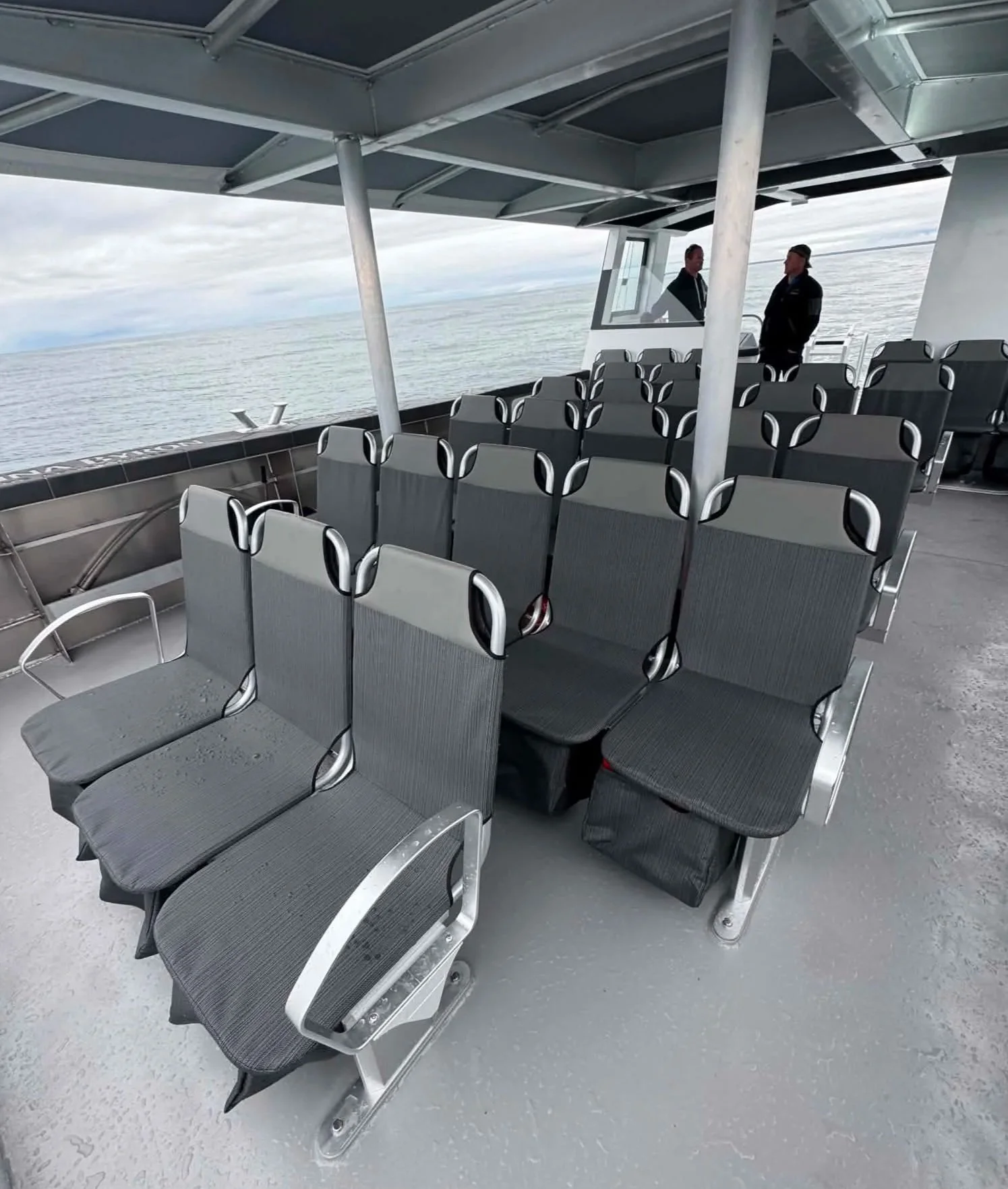 Passenger / ferry seating area on a boat with rows of weatherproof gray fabric seats, lifejacket holders under the seats on a metal frame. Large volume seating for passengers or crew onboard a custom designed catamaran. Signature design.