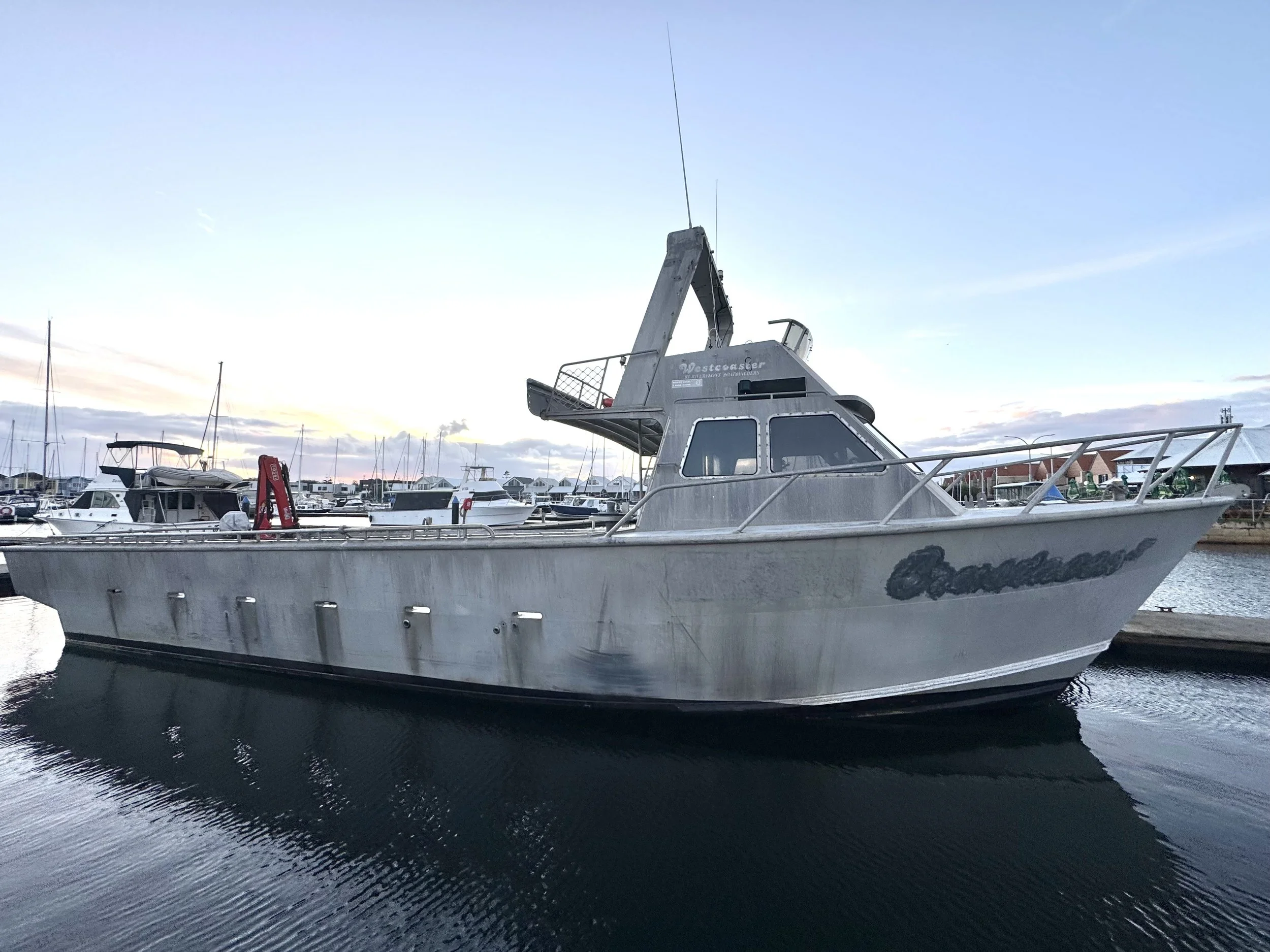 A silver boat named 'Orlando' docked in a marina with other boats in the background, during sunset.
