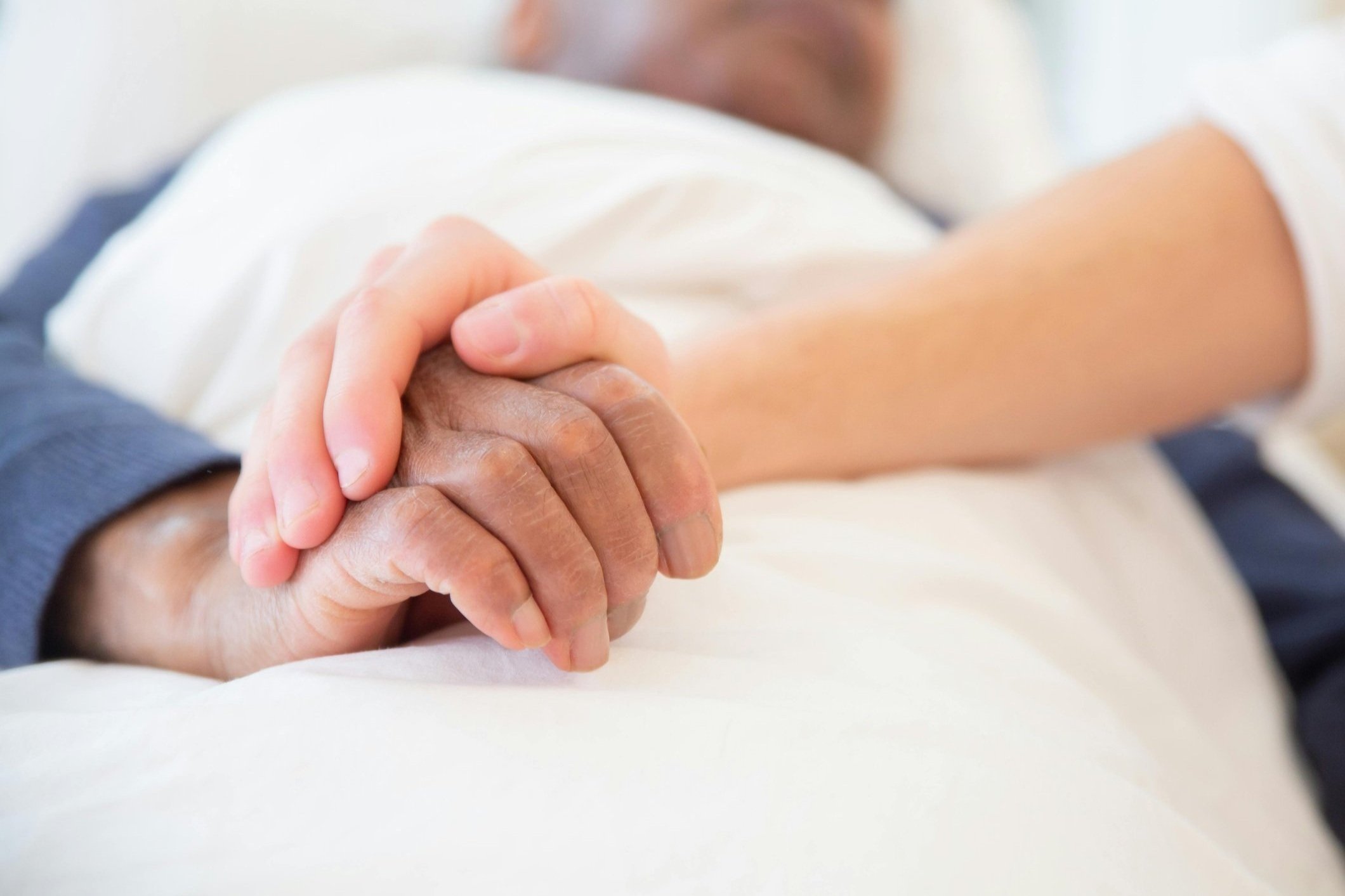Close-up of elderly couple holding hands on a bed, emphasizing connection and support.
