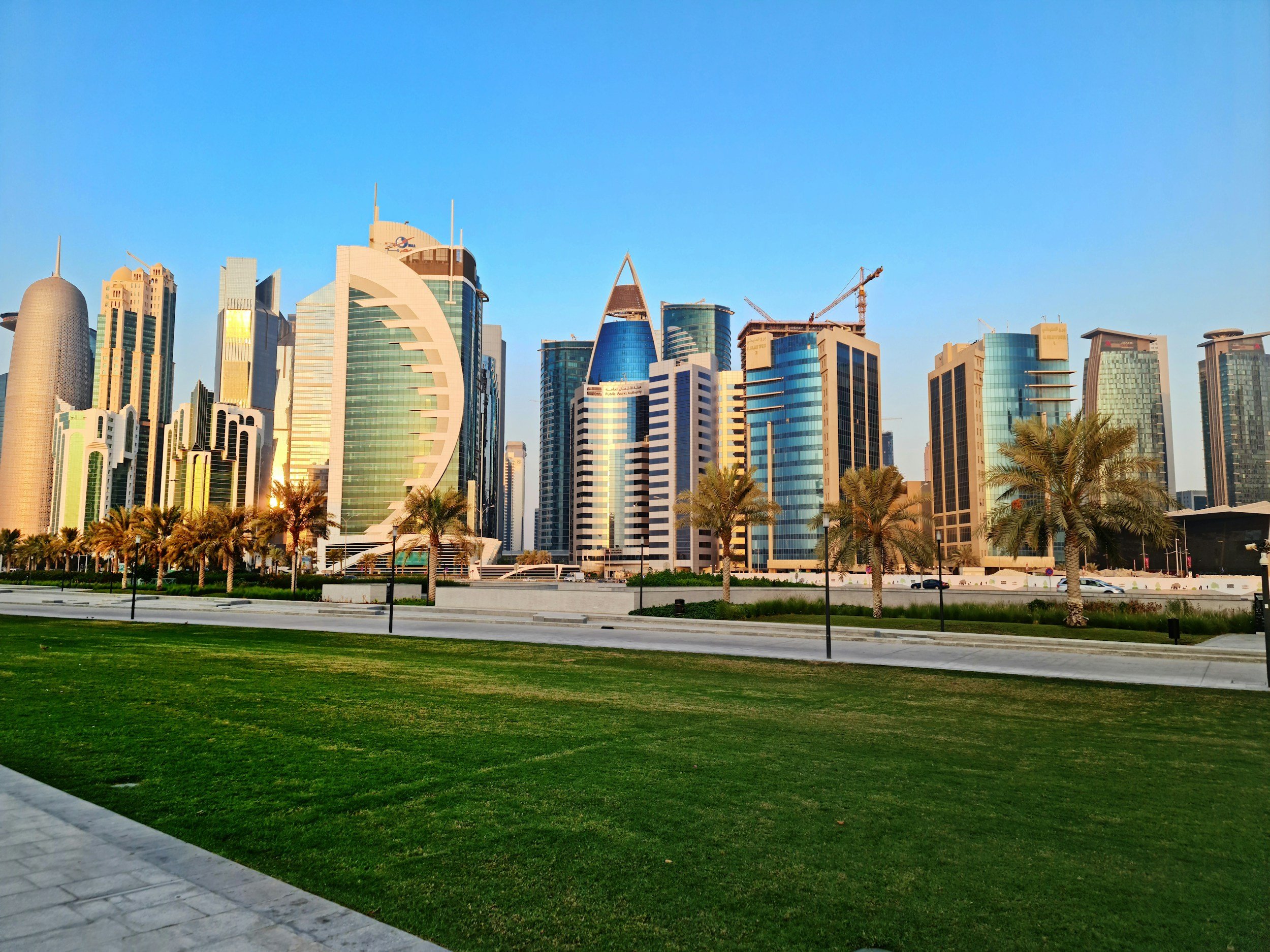 Skyline of Doha, Qatar with modern skyscrapers and palm trees, under a clear blue sky.