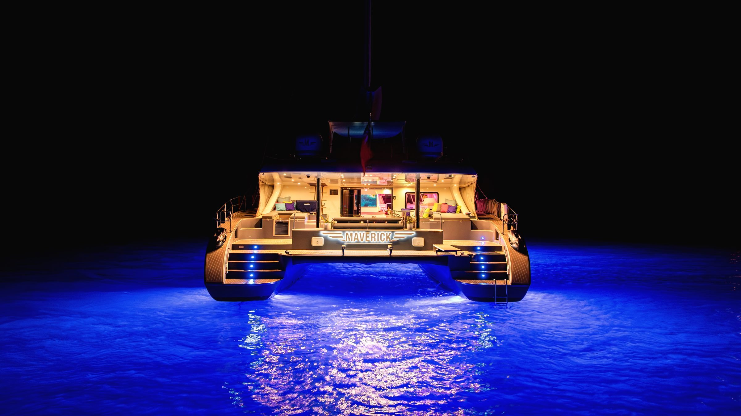 MAVERICK's stern at night with the aft deck lit and blue underwater lights on the water, BVI.