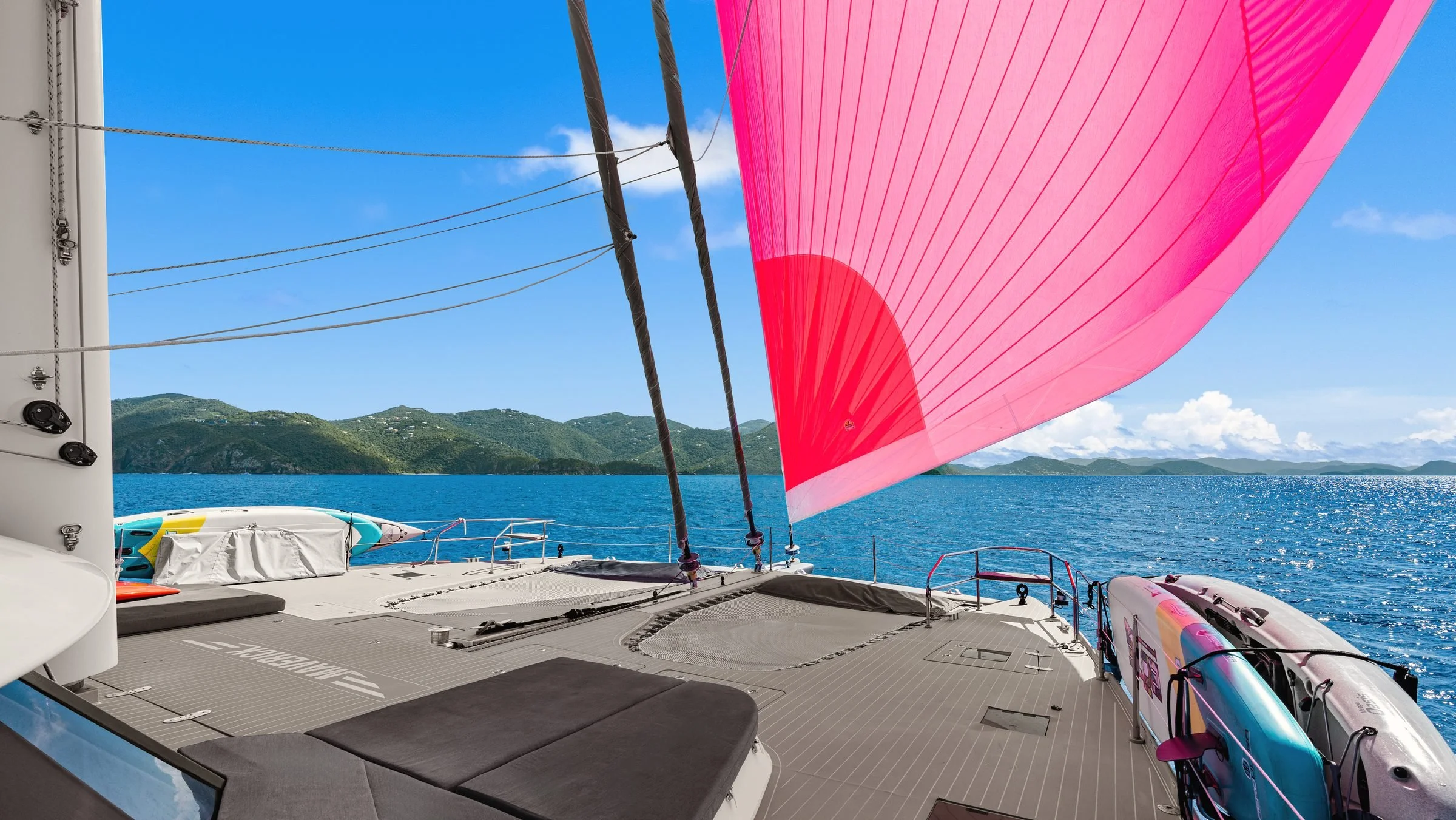 MAVERICK's foredeck under her pink spinnaker, with green hills across the water, BVI.