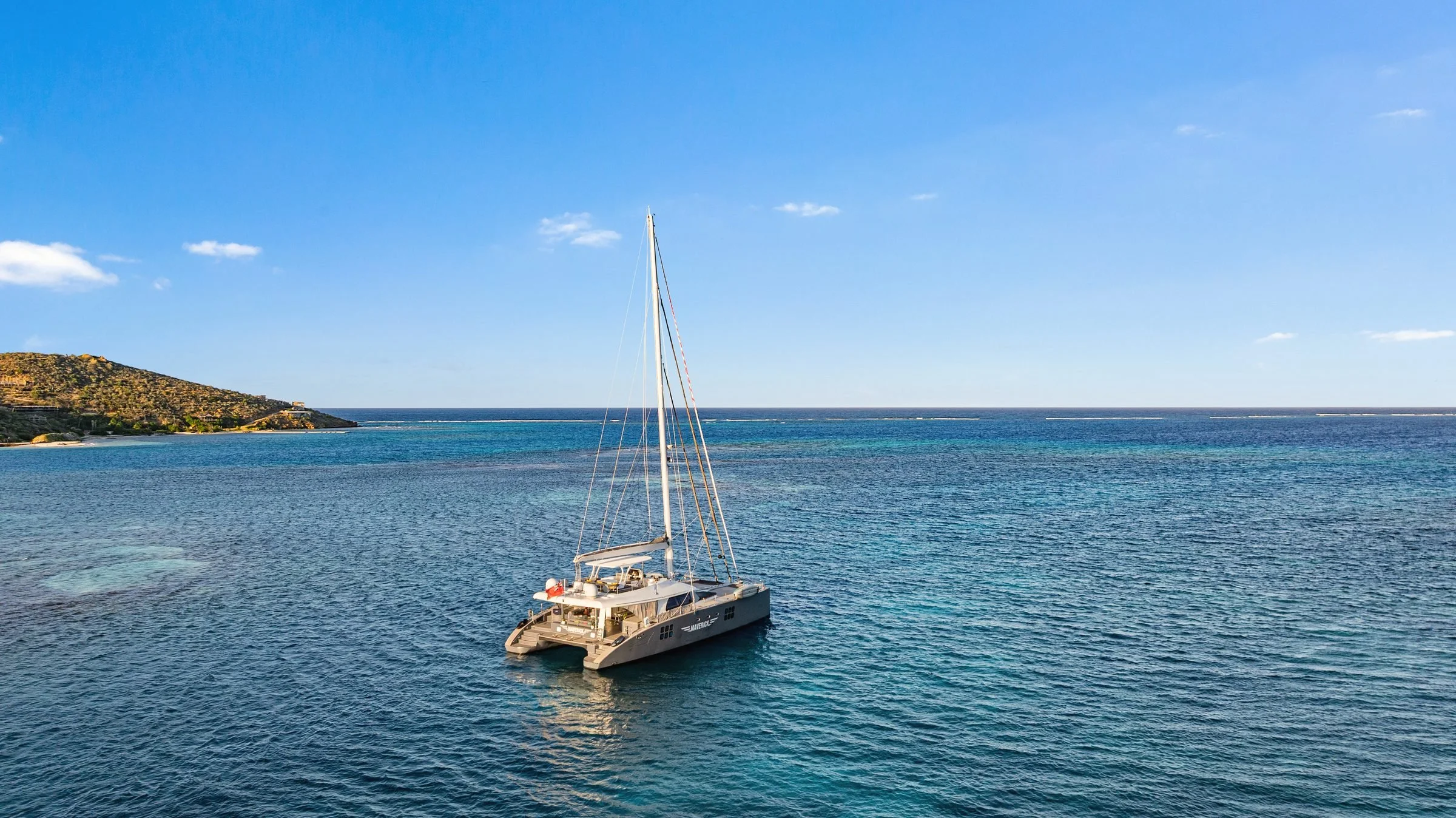 MAVERICK at anchor in deep blue water off a green headland, BVI.