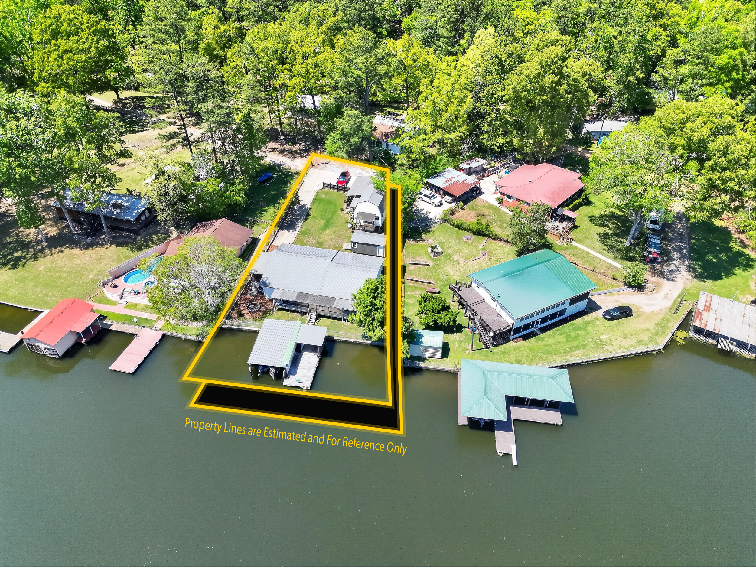 An aerial view of a residential area along a waterway with houses on stilts. Some houses have boats docked nearby, and lush green trees surround the properties. Property lines are highlighted in yellow, with a disclaimer about estimated lines.