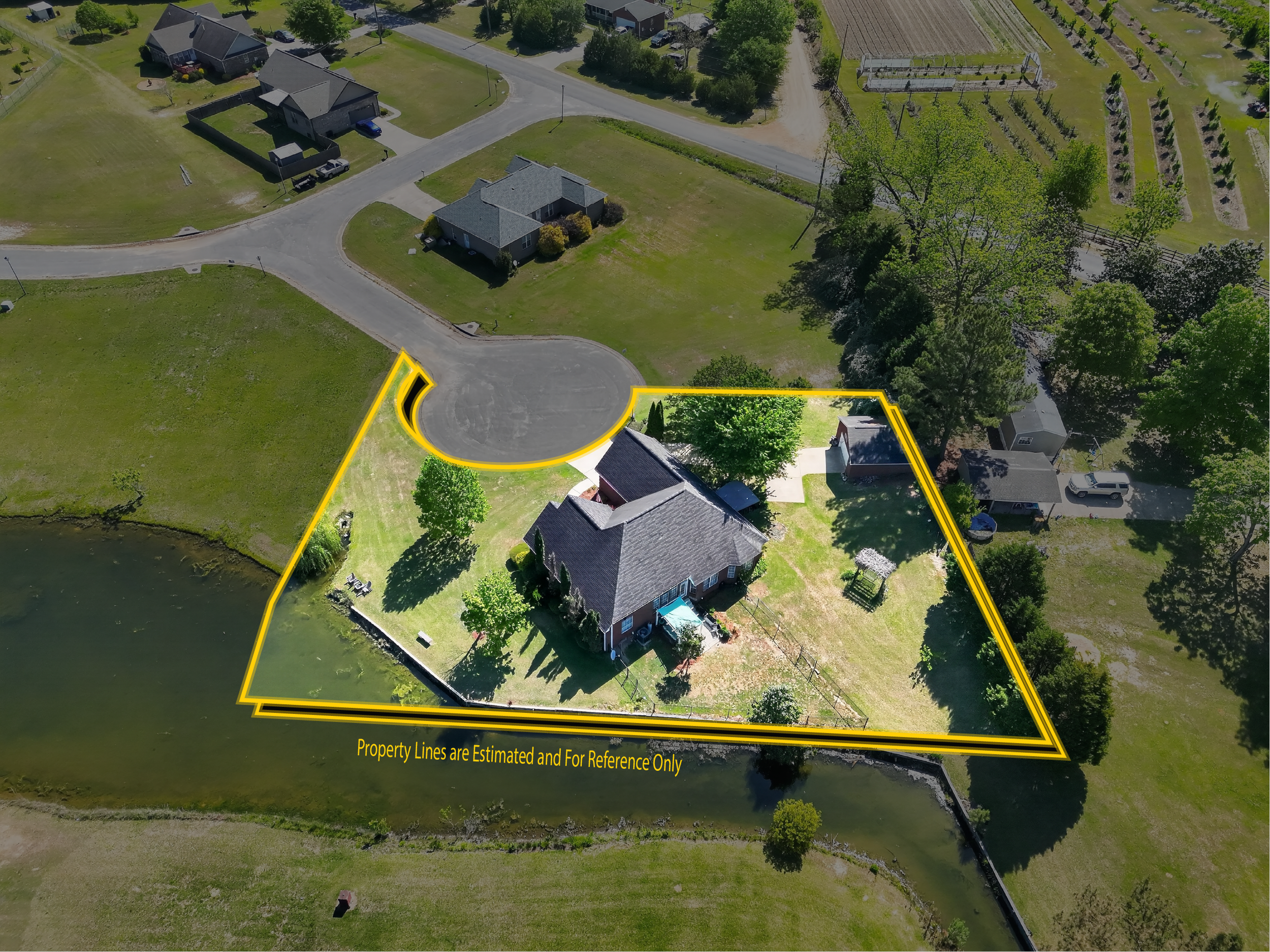 Aerial view of a residential area with houses, a pond, and green lawns. Property lines are outlined in yellow, with a note indicating they are estimated and for reference only.
