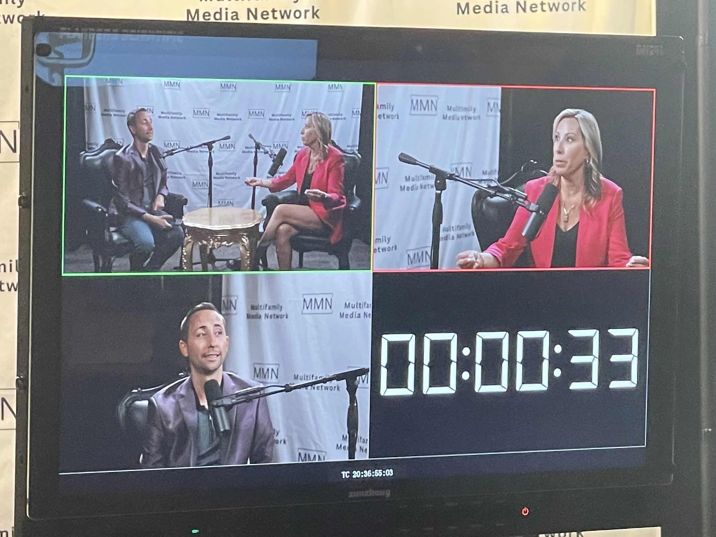Video production monitor showing three people in a radio or podcast interview setting, with a digital timer displaying 00:00:33.
