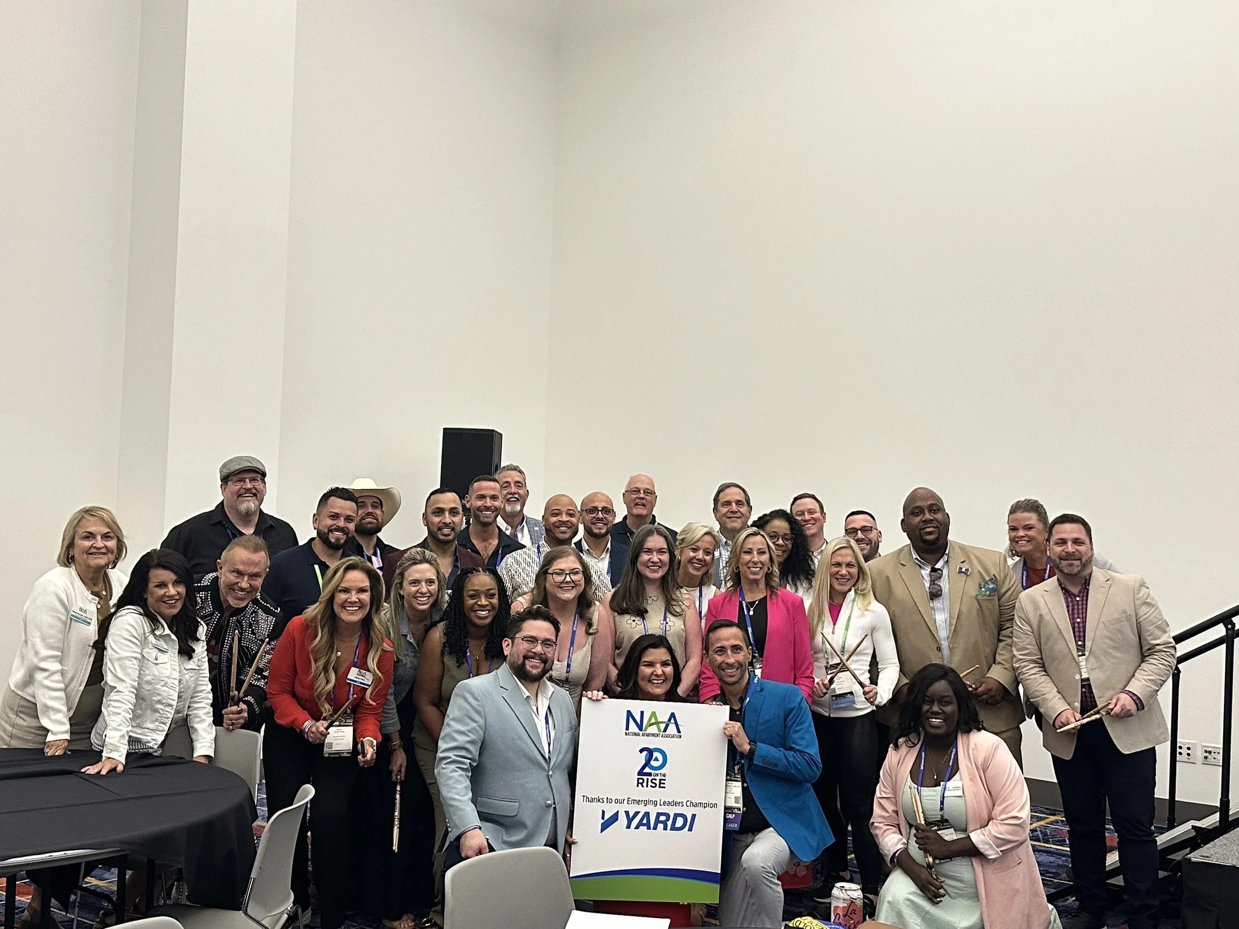Group of diverse people at an indoor conference, holding a Yardi-branded sign, smiling for a group photo.
