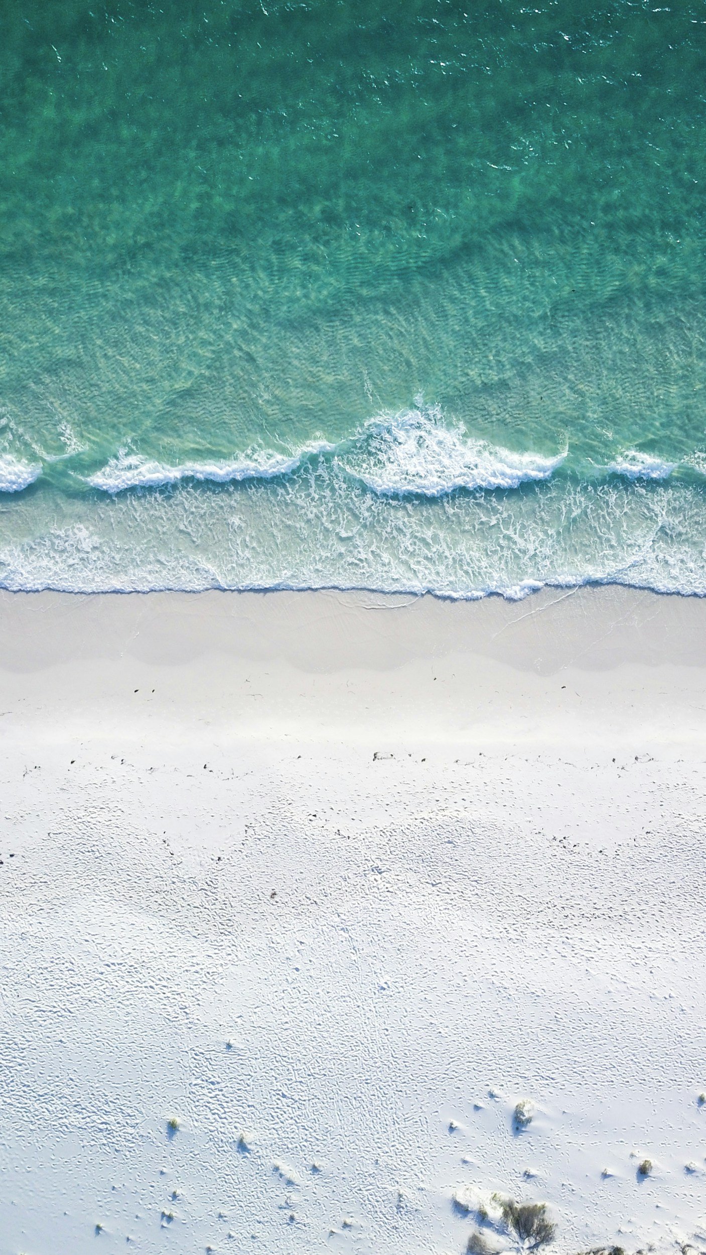 aerial view of a beach with white sand, gentle waves, and turquoise ocean water