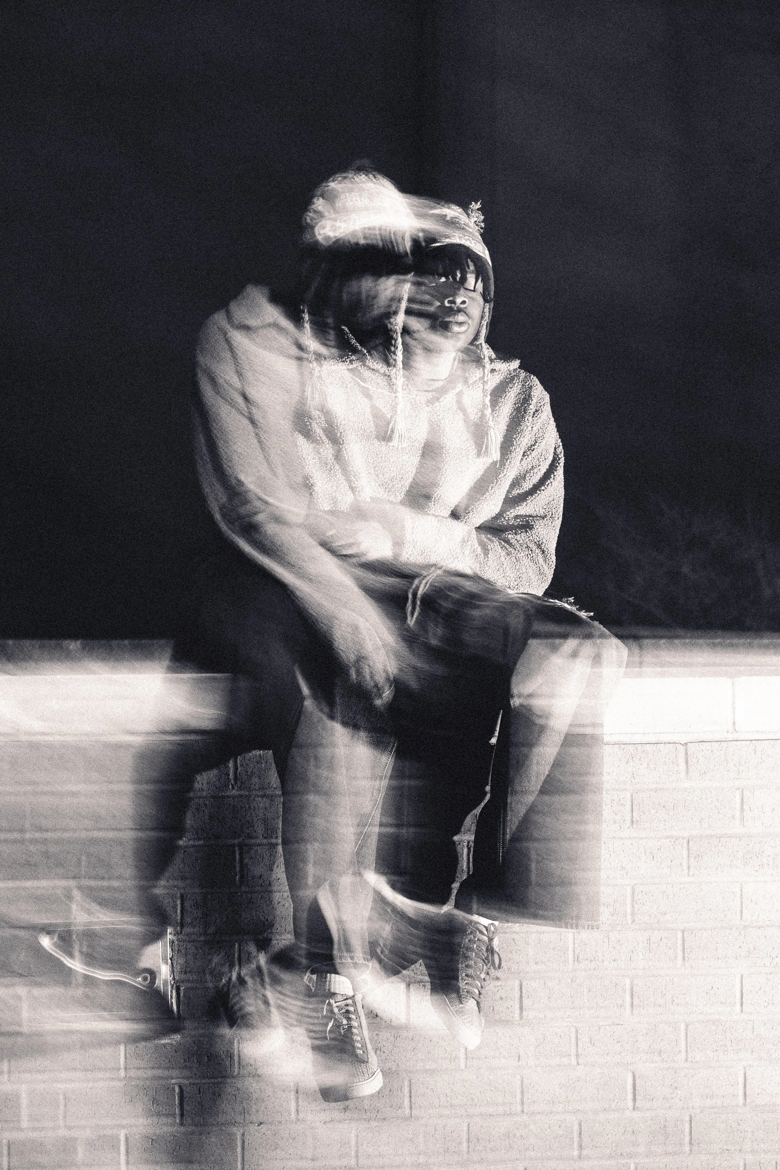 Black and white photo of a person sitting on a brick wall, with a blurred motion effect.