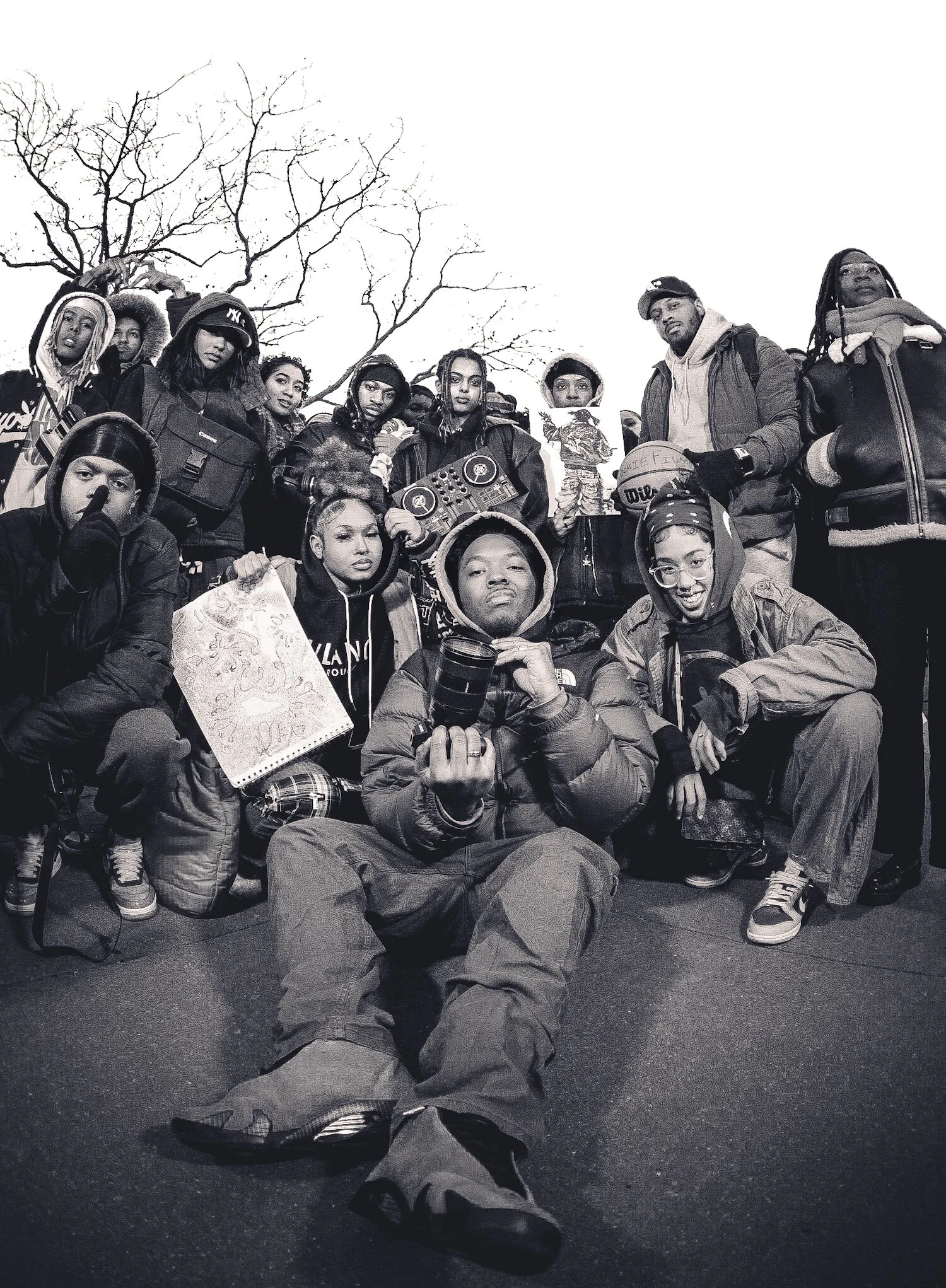 Group of diverse young people outdoors, some wearing jackets, with a leafless tree in the background, posing for a black and white photo.