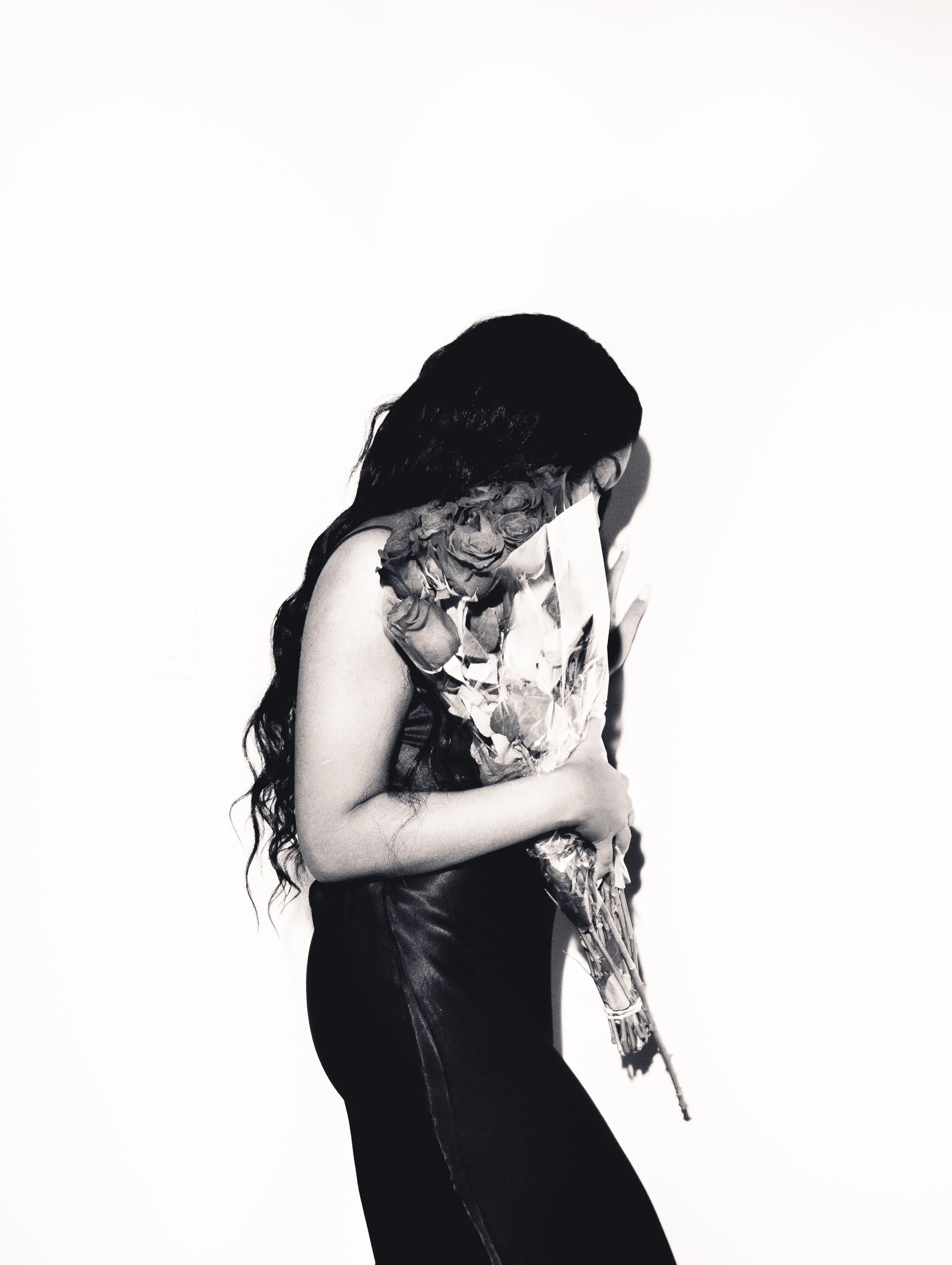 A woman with long dark hair holding a large bouquet of roses, standing against a white background.