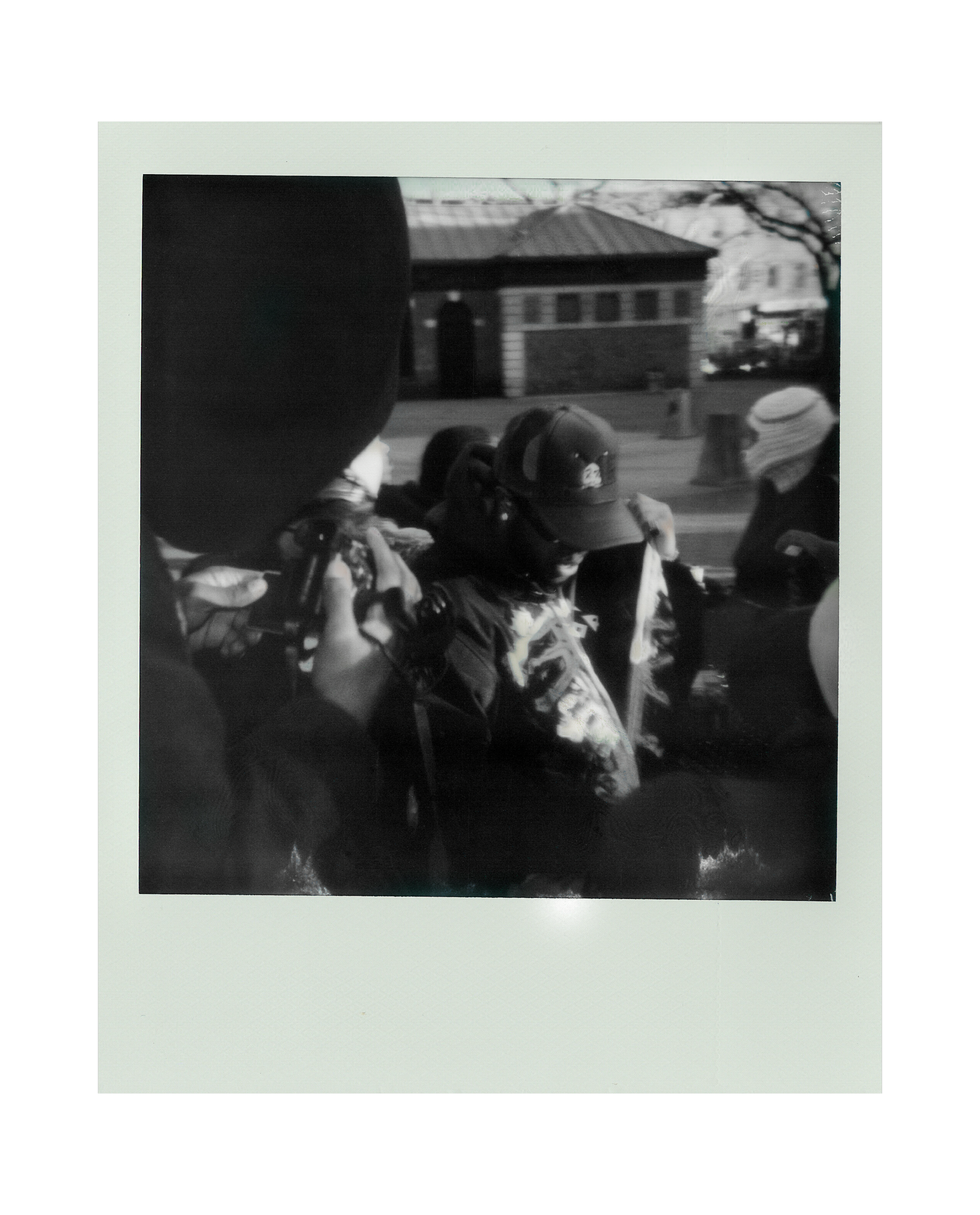 Black and white photograph of a group of people, some wearing helmets, gathered outdoors with a building in the background.