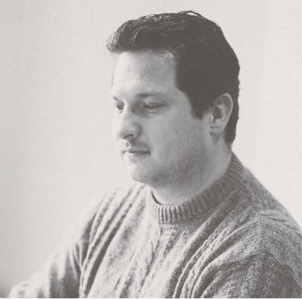 Caleb Blackford, co-principal of The Blackfjord, in black and white profile portrait, wearing a grey cable knit sweater, gaze forward in thought.
