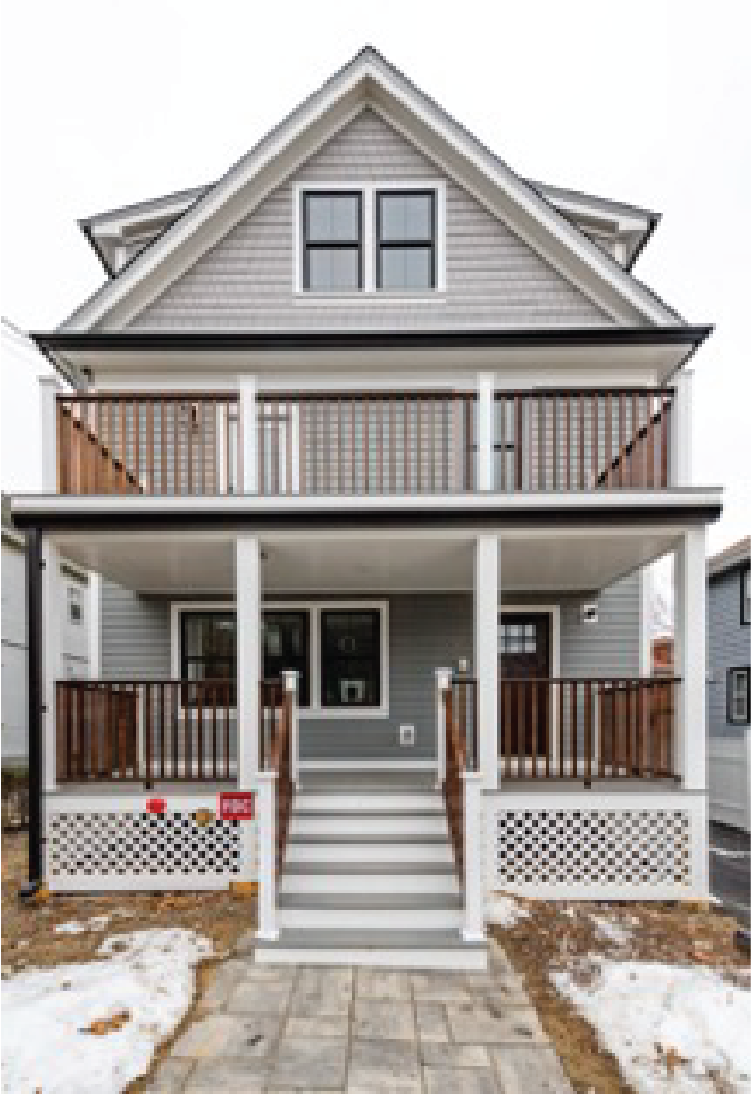 Two-story gray house with a gable roof, wooden balcony, and front porch.