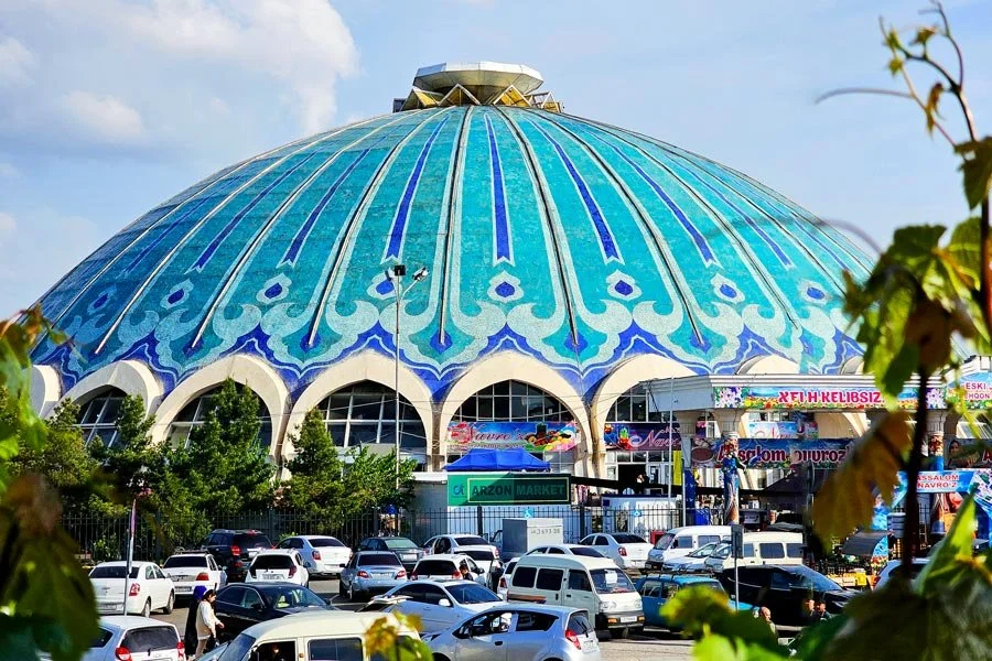 A large, dome-shaped building with colorful blue and turquoise patterns on its exterior, surrounded by a parking lot with cars and some trees in the foreground.