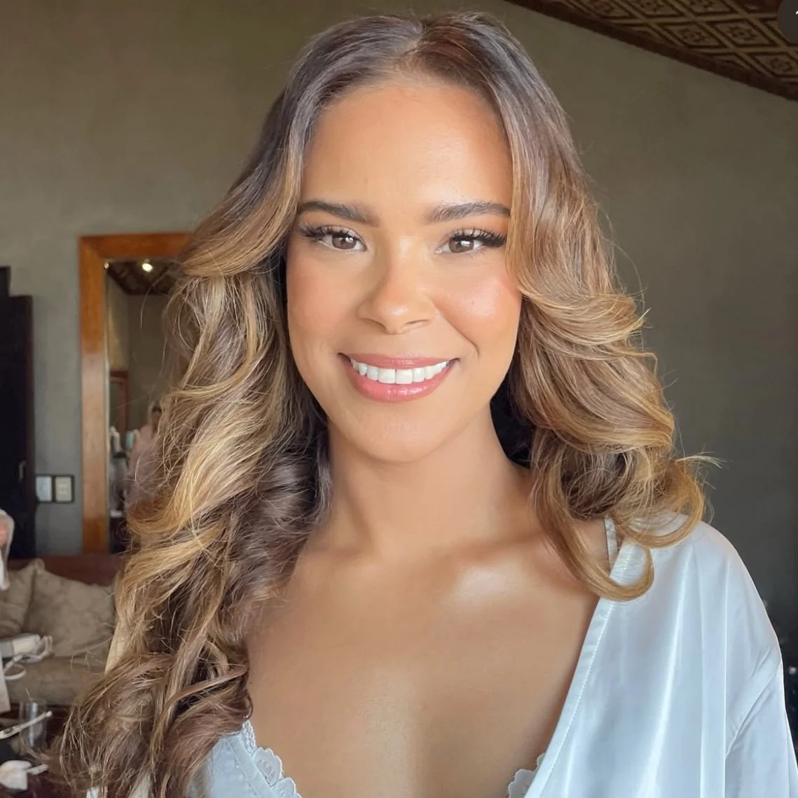 Smiling woman with long, wavy hair wearing a white robe indoors.