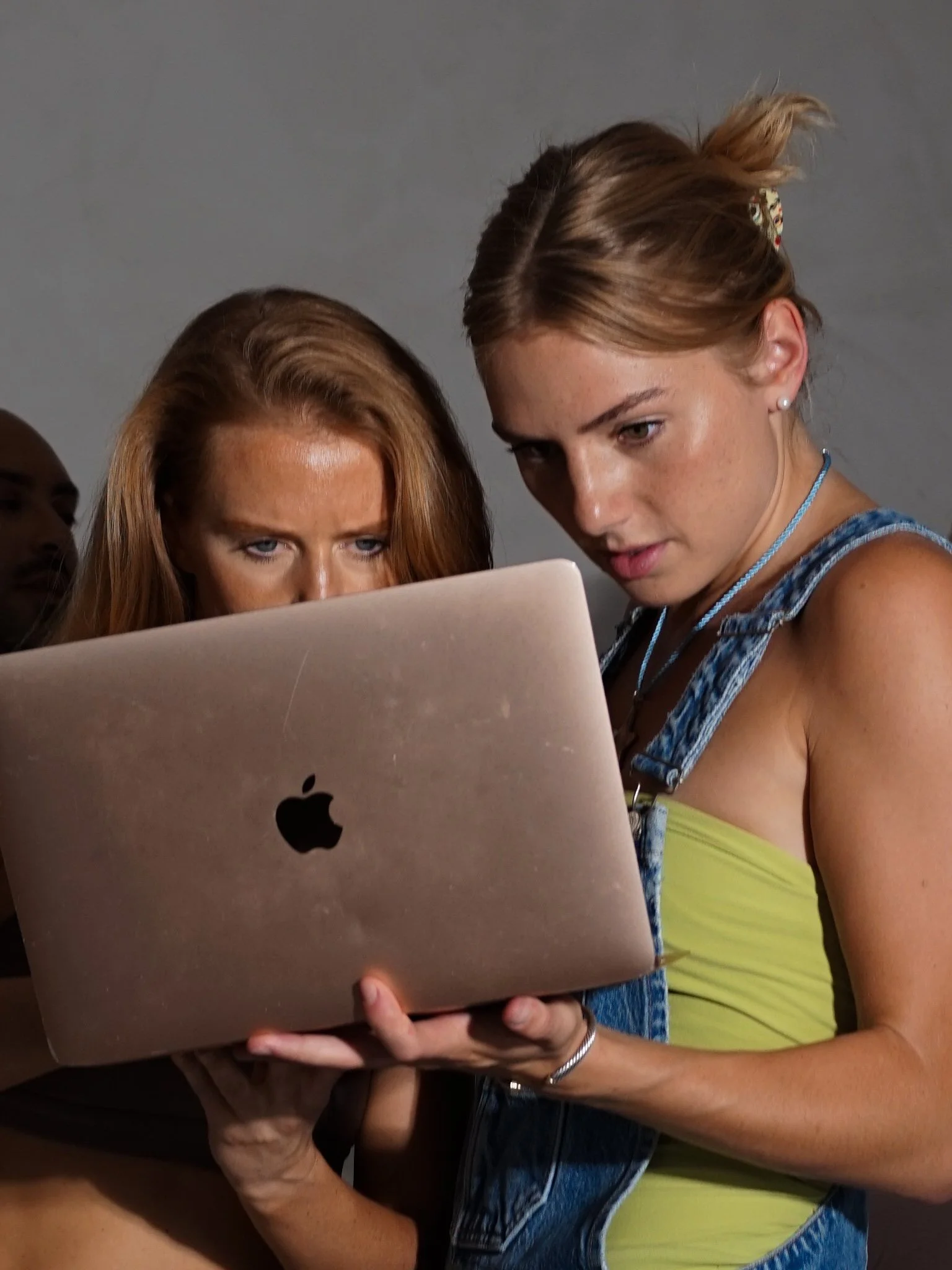 Two young women looking intently at a laptop screen, with a gray background.