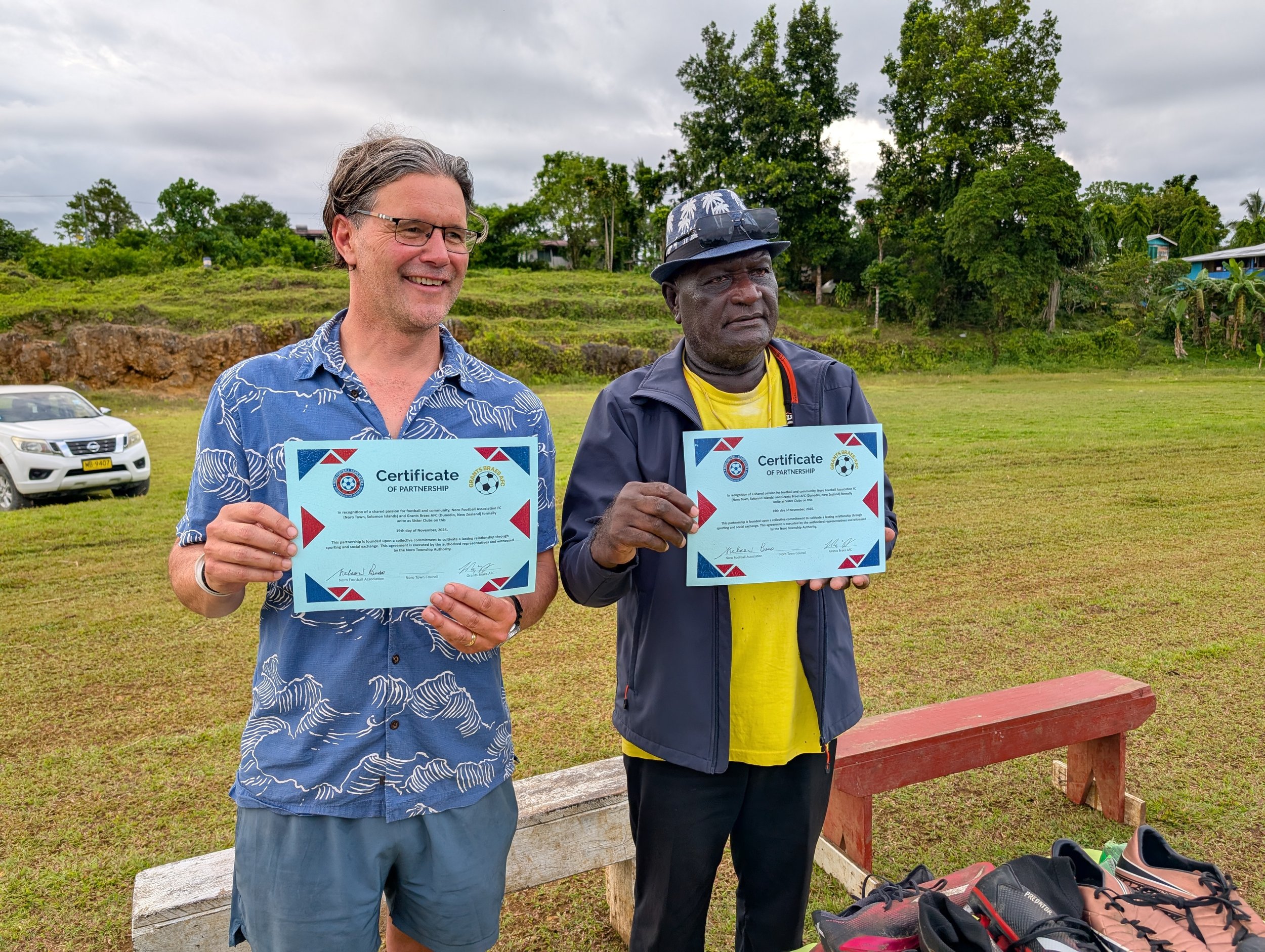 Lloyd and Nelson holding up their Certificate of Partnership - formally uniting Noro Football Association FC and Grants Braes AFC as sister clubs.