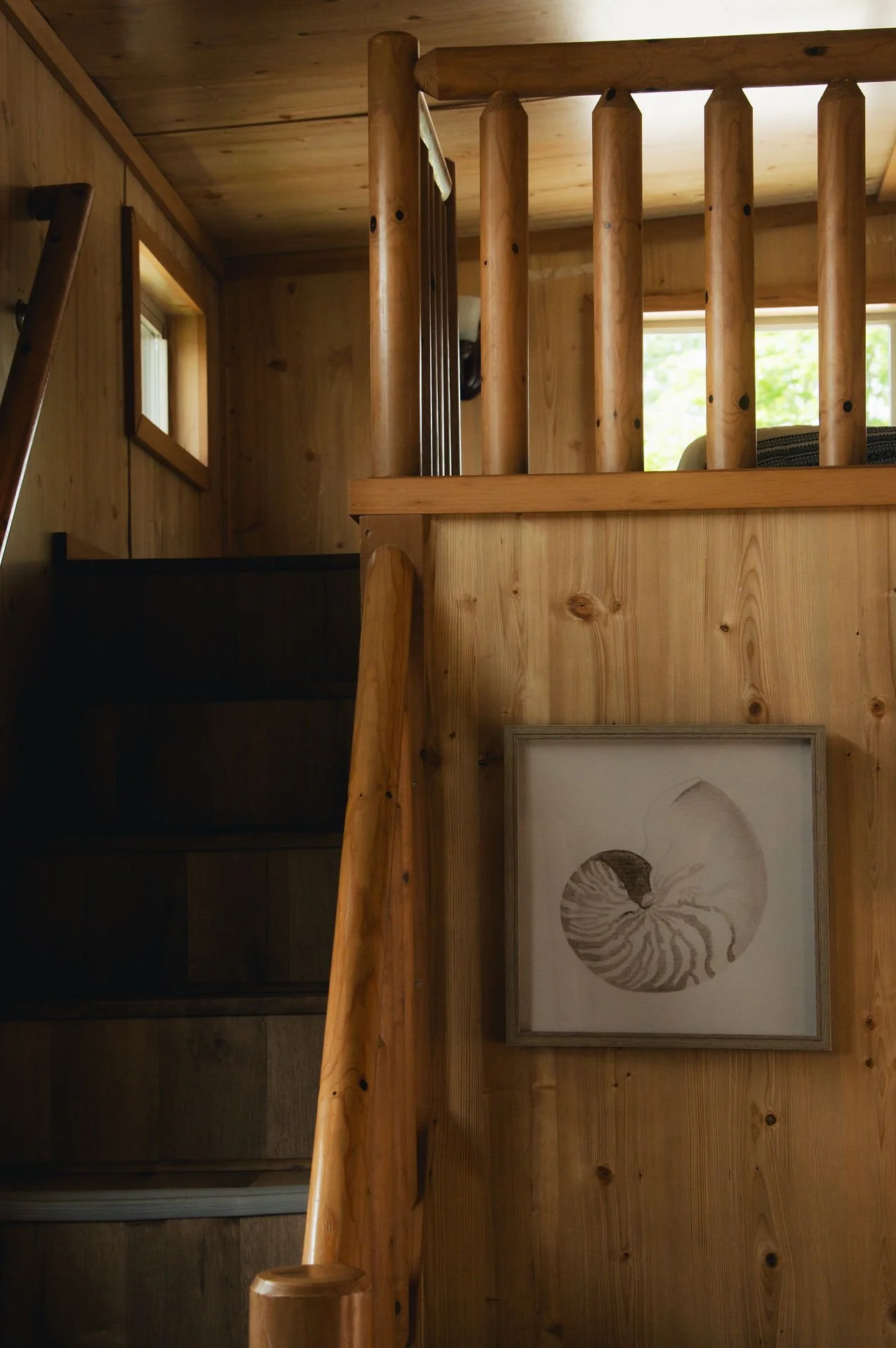 Interior view of a wooden staircase with logs, featuring a framed drawing of a nautilus shell on the wall.