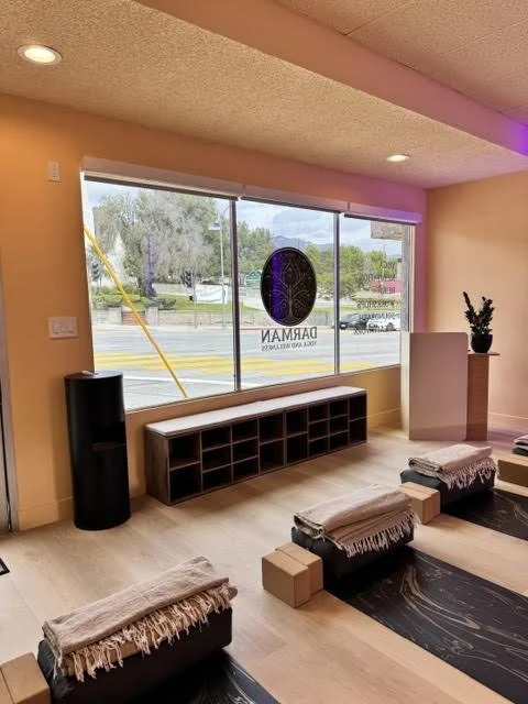 Interior of a yoga studio with mats, cushions, blankets, and a window with a view of the street.