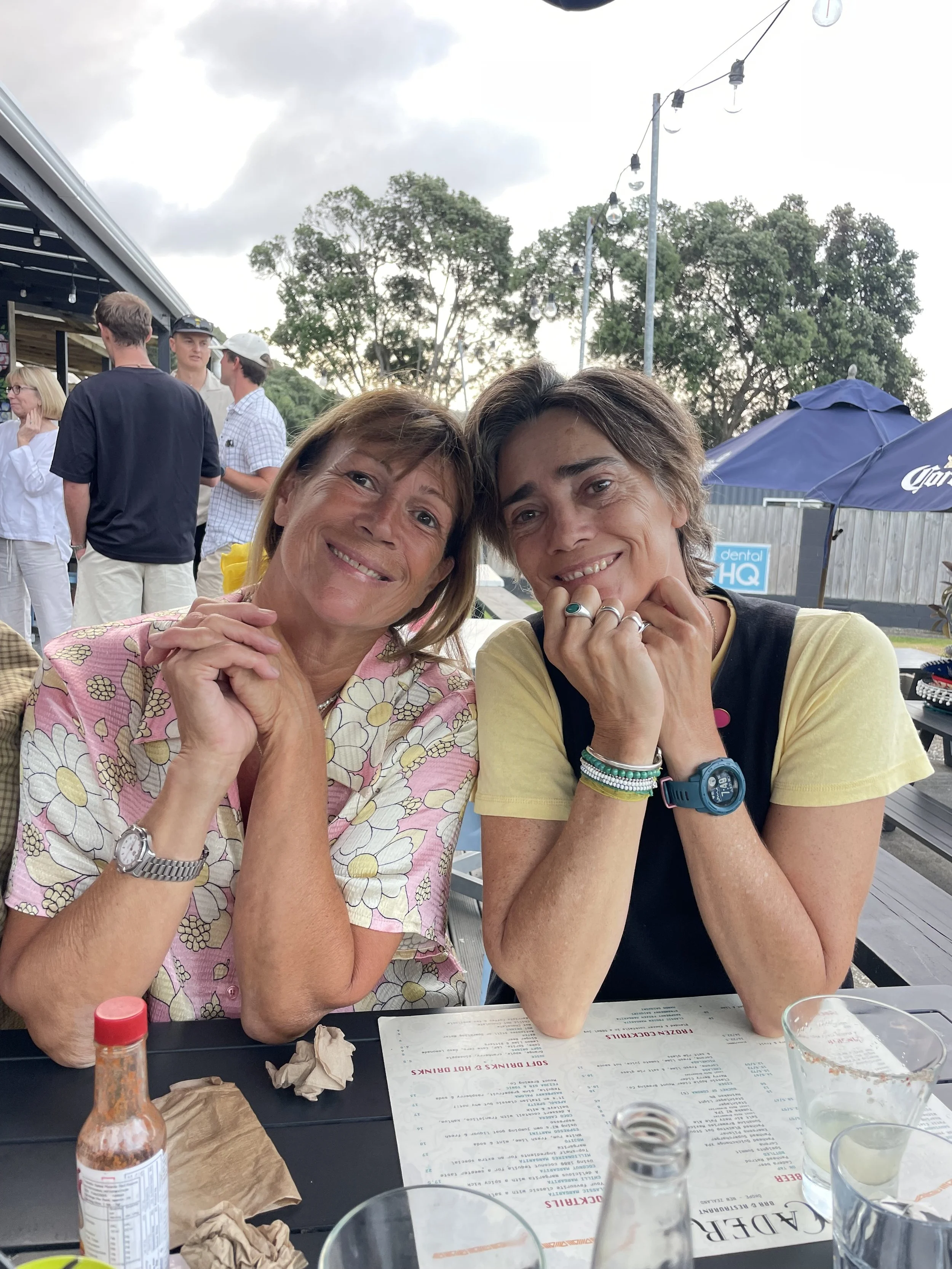Two brown haired women in midlife sitting side by side with their heads touching. They are sisters.