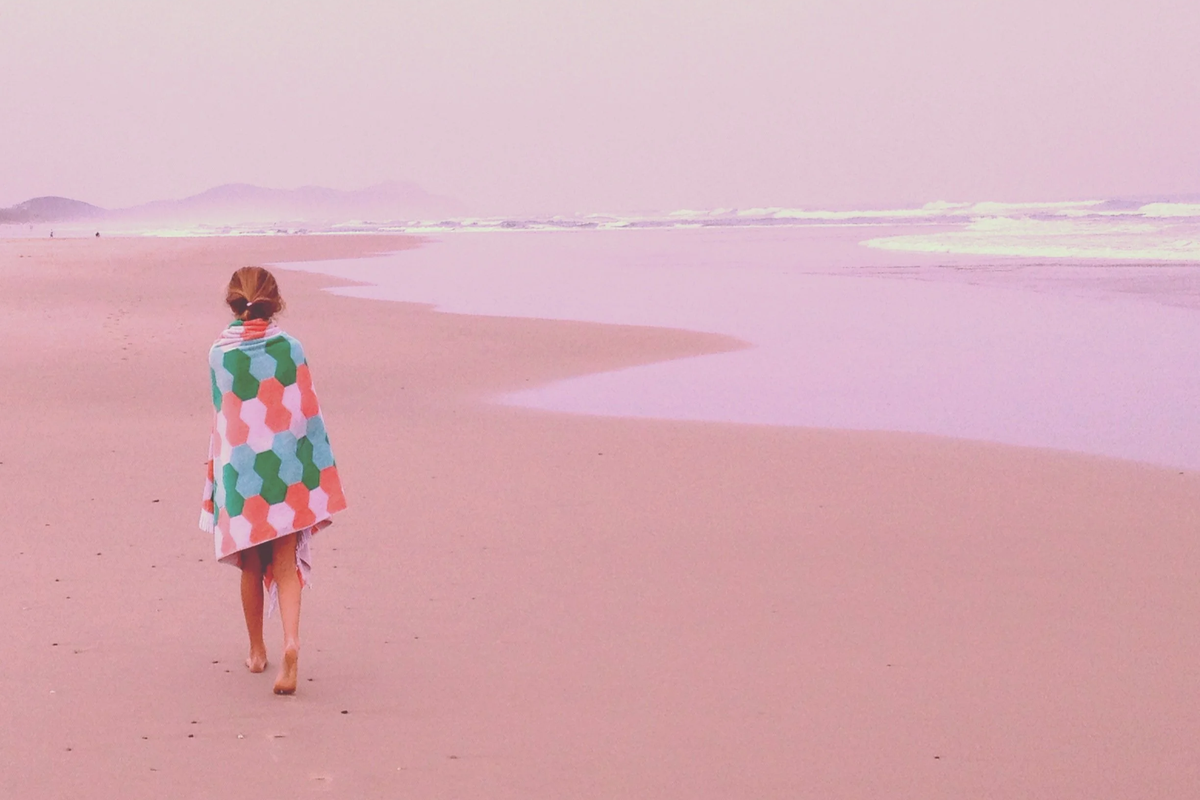Girl wrapped in towel walking away down a beautiful empty beach in Bondi Bay
