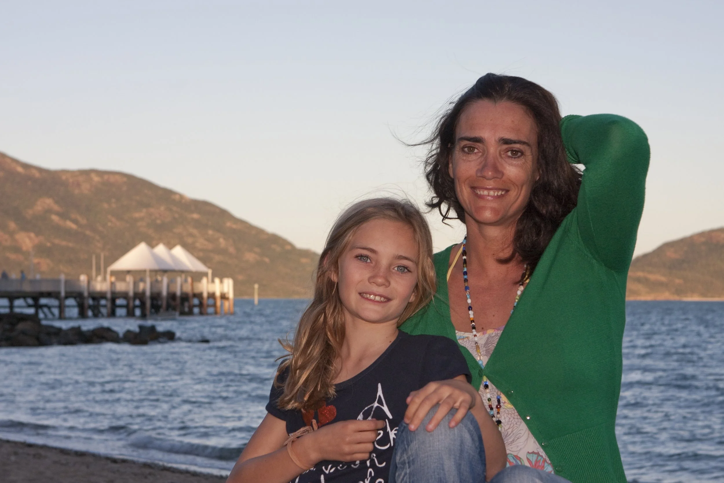 Woman in green cardigan cuddling young girl 10 years old with blonde hair. Mum and daughter.