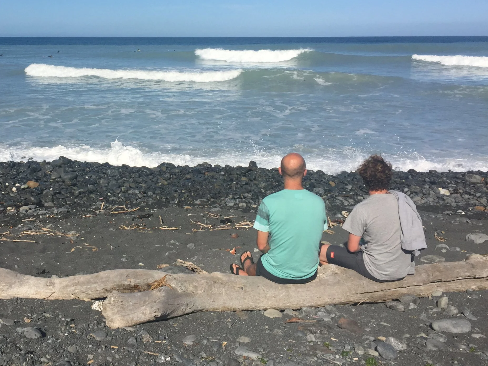 Adult and teenager sitting on a beach looking out to sea in contemplation.
