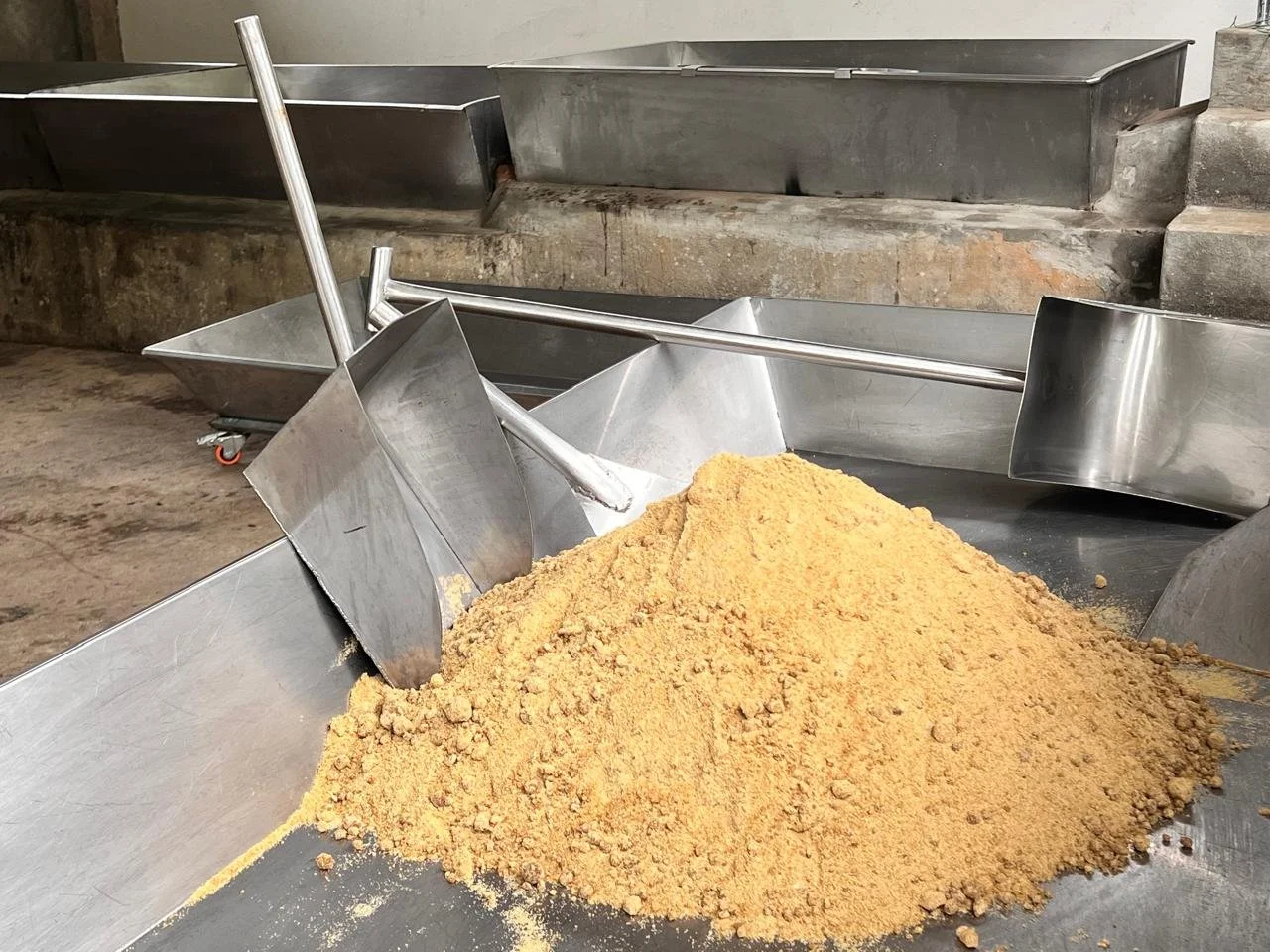 Panela granulada en una bandeja de metal grande con palas metálicas cerca.