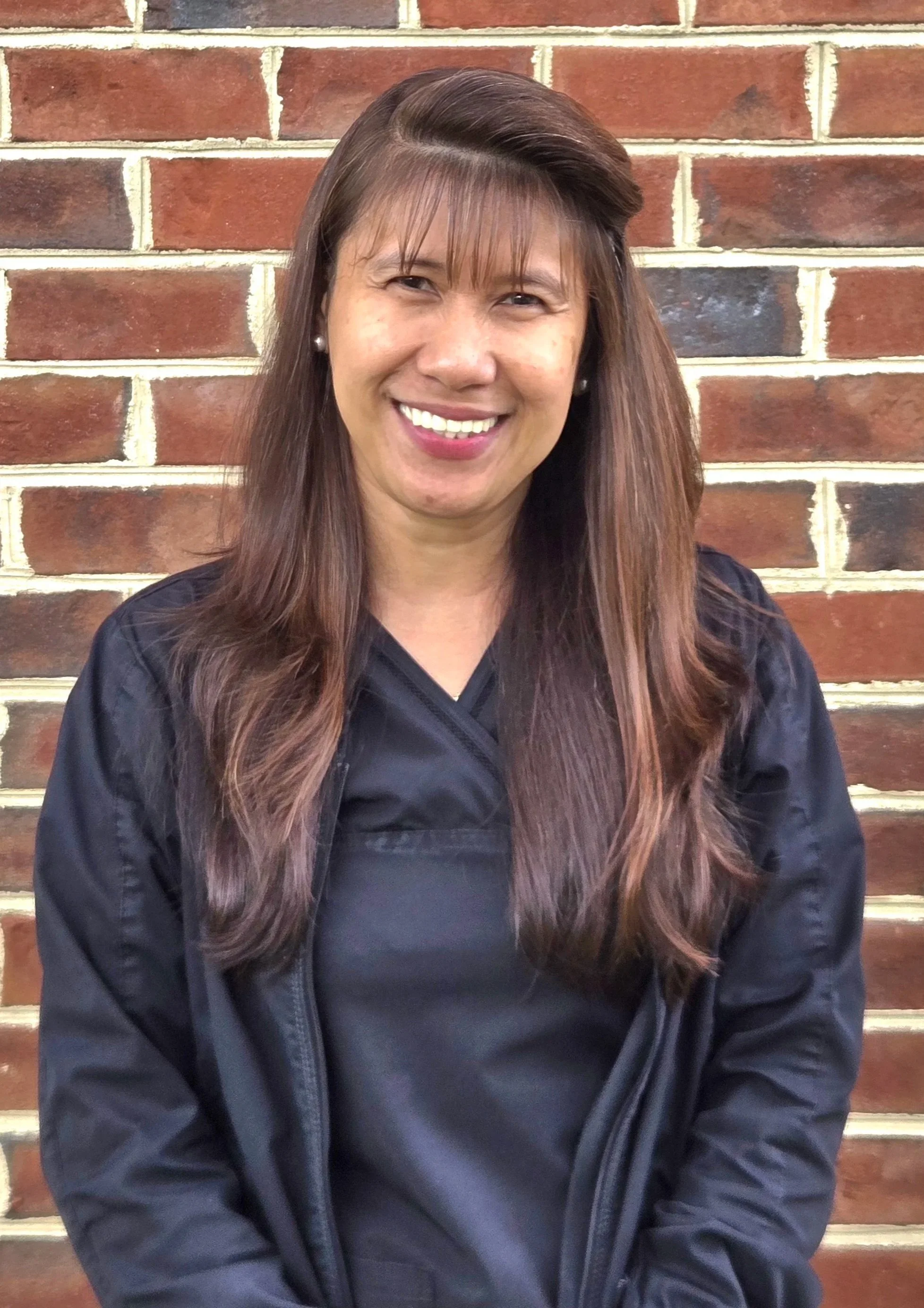 A woman, with long hair, smiling and standing against a brick wall.