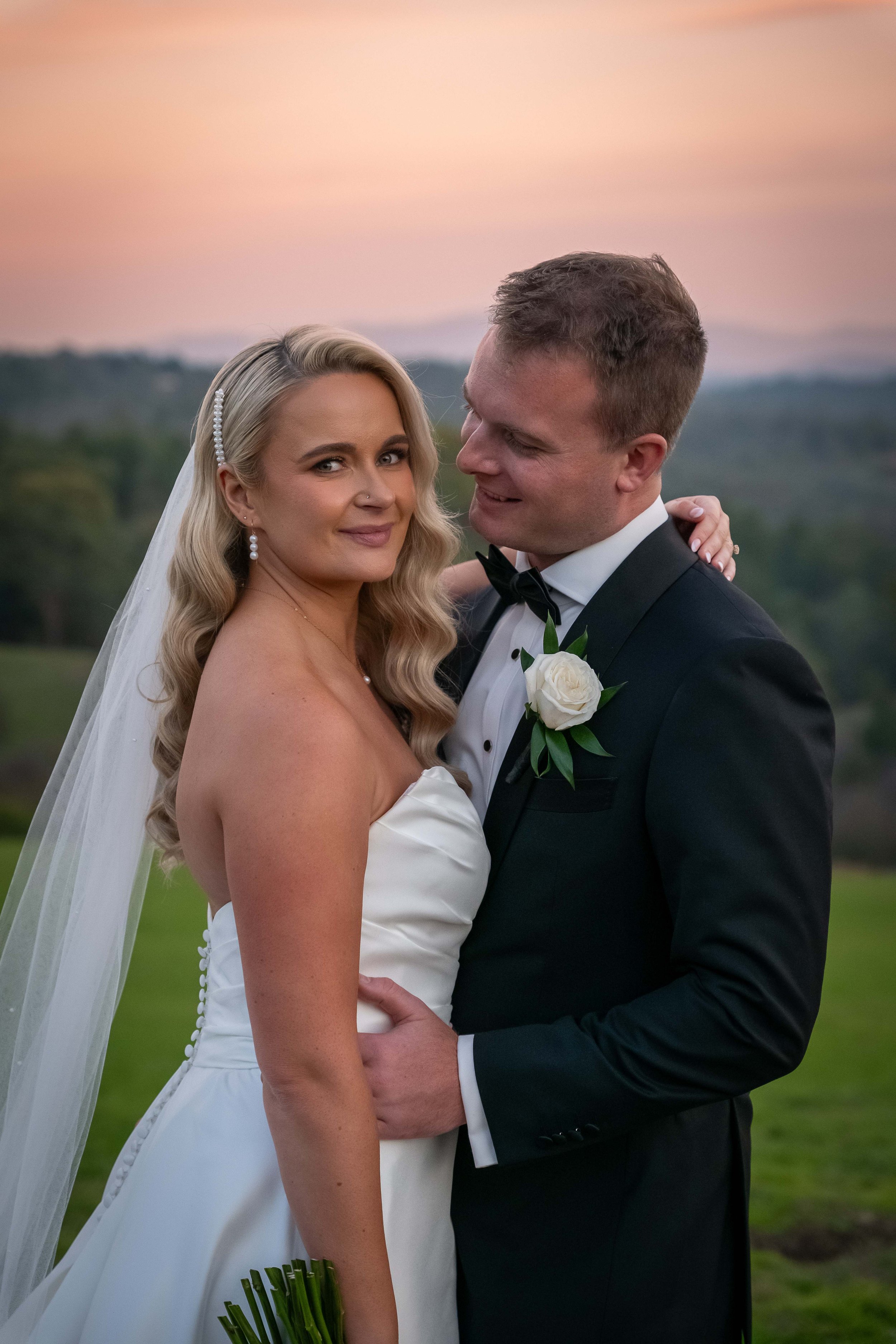 Bride and groom embracing outdoors with sunset background.