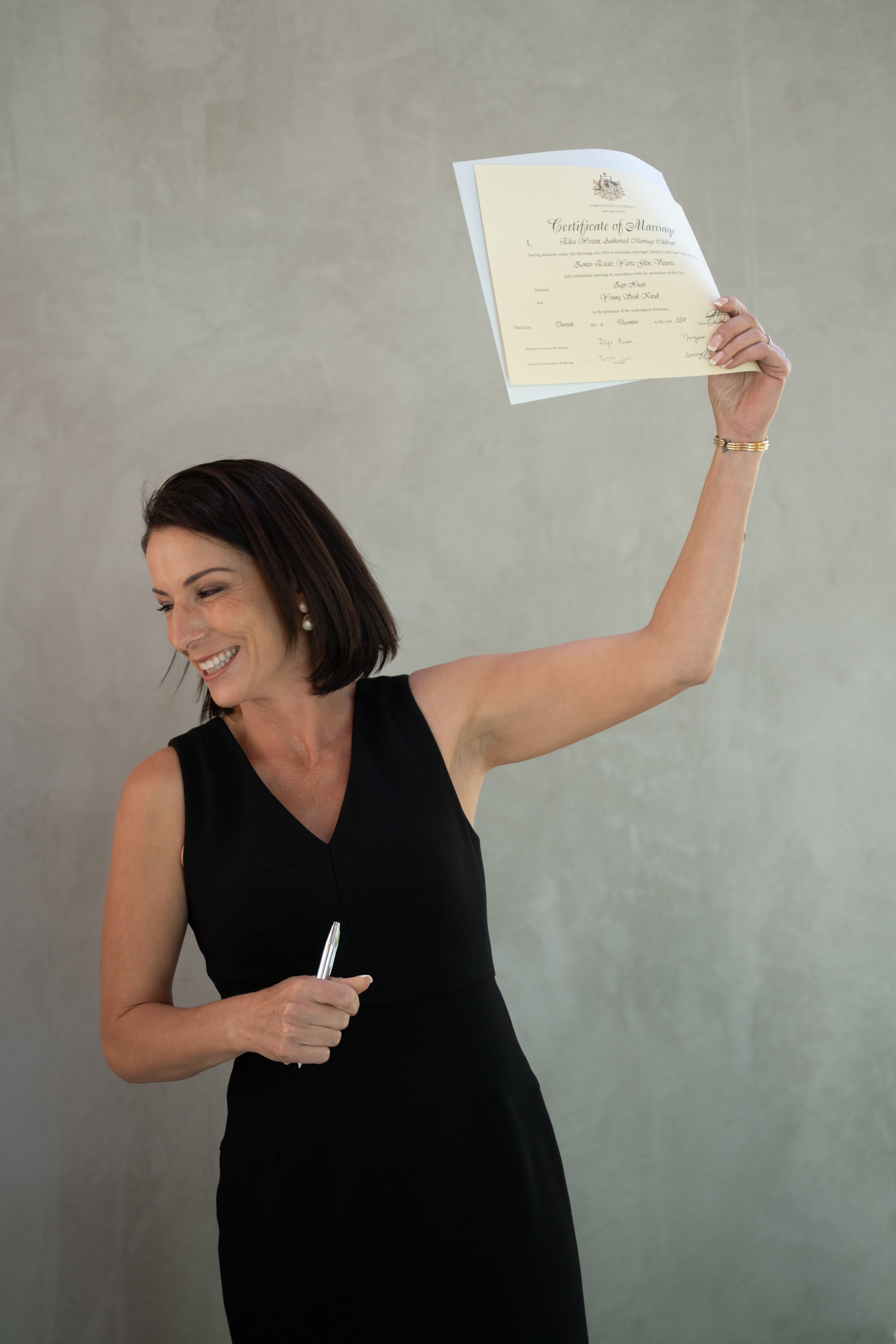 Celebrant holding a marriage certificate and a pen, smiling.