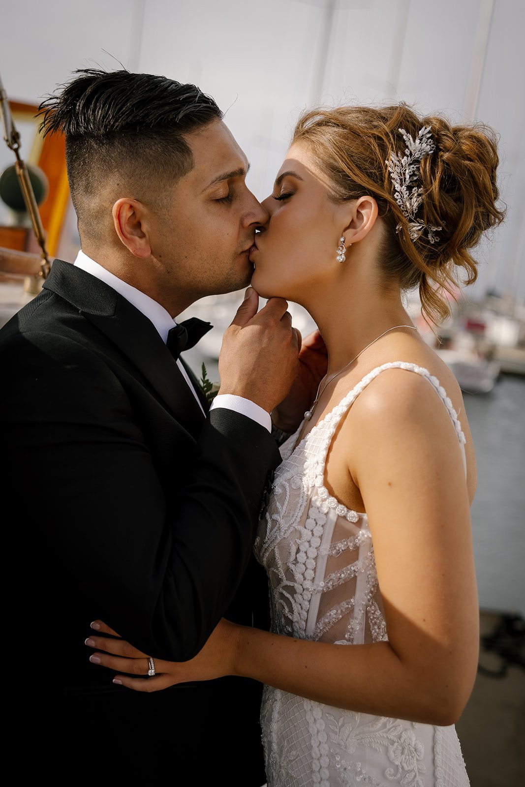 Bride and groom kissing in wedding attire on a boat.