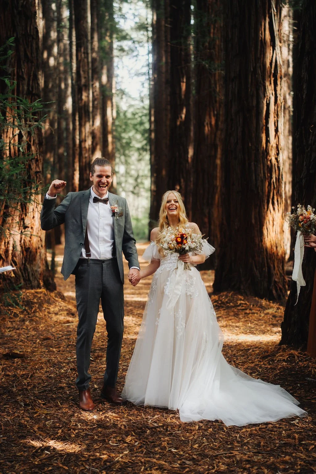 A couple standing in a forest with tall redwood trees.