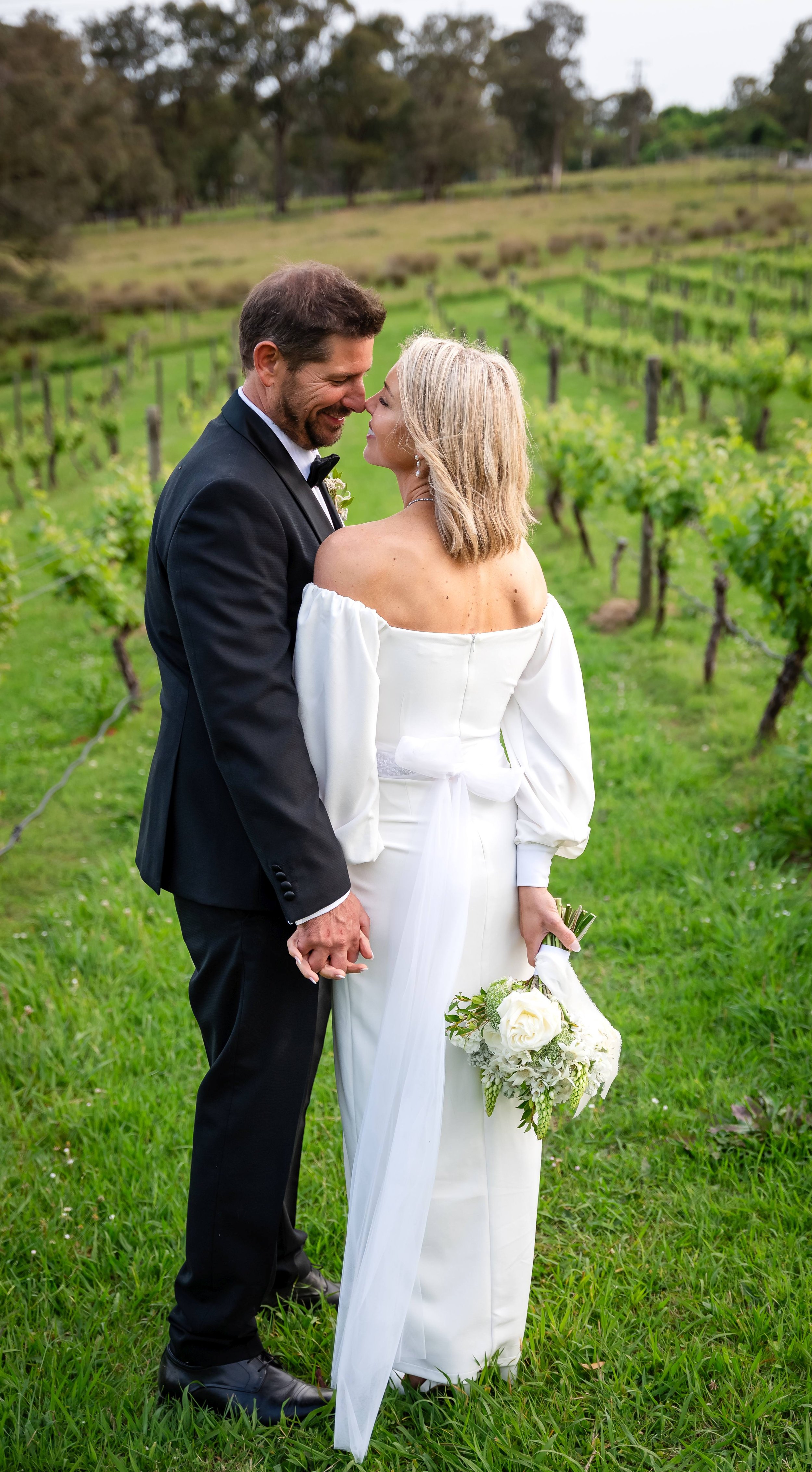 Bride and groom embracing in a vineyard, bride holding a bouquet.