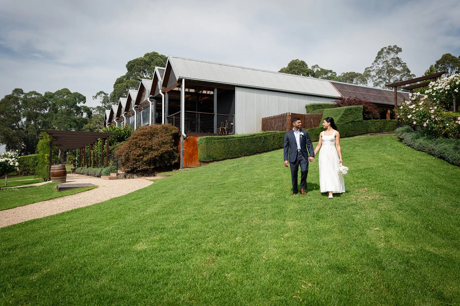 Wedding couple walking down aisle outdoors, smiling with flower petals in the air.