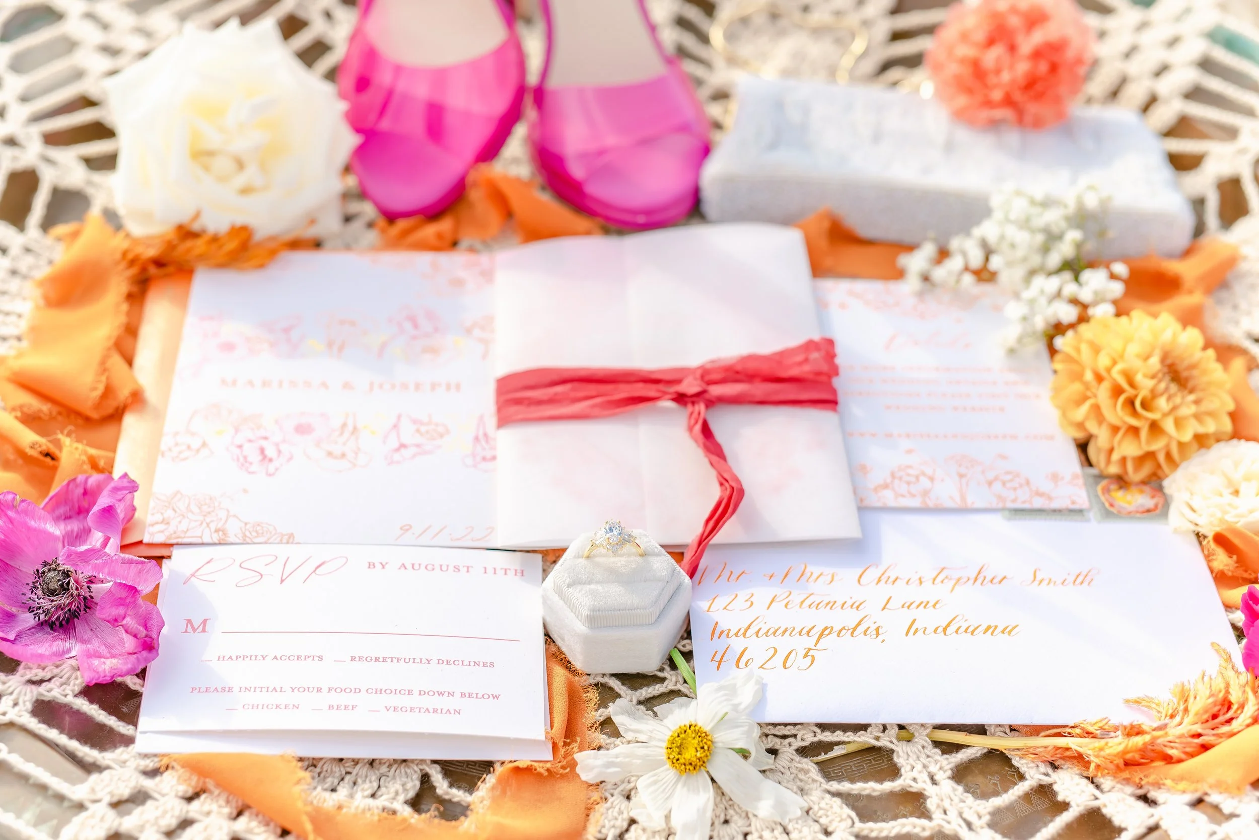 Wedding invitation suite with RSVP card, pink shoes, floral decorations, and engagement ring.