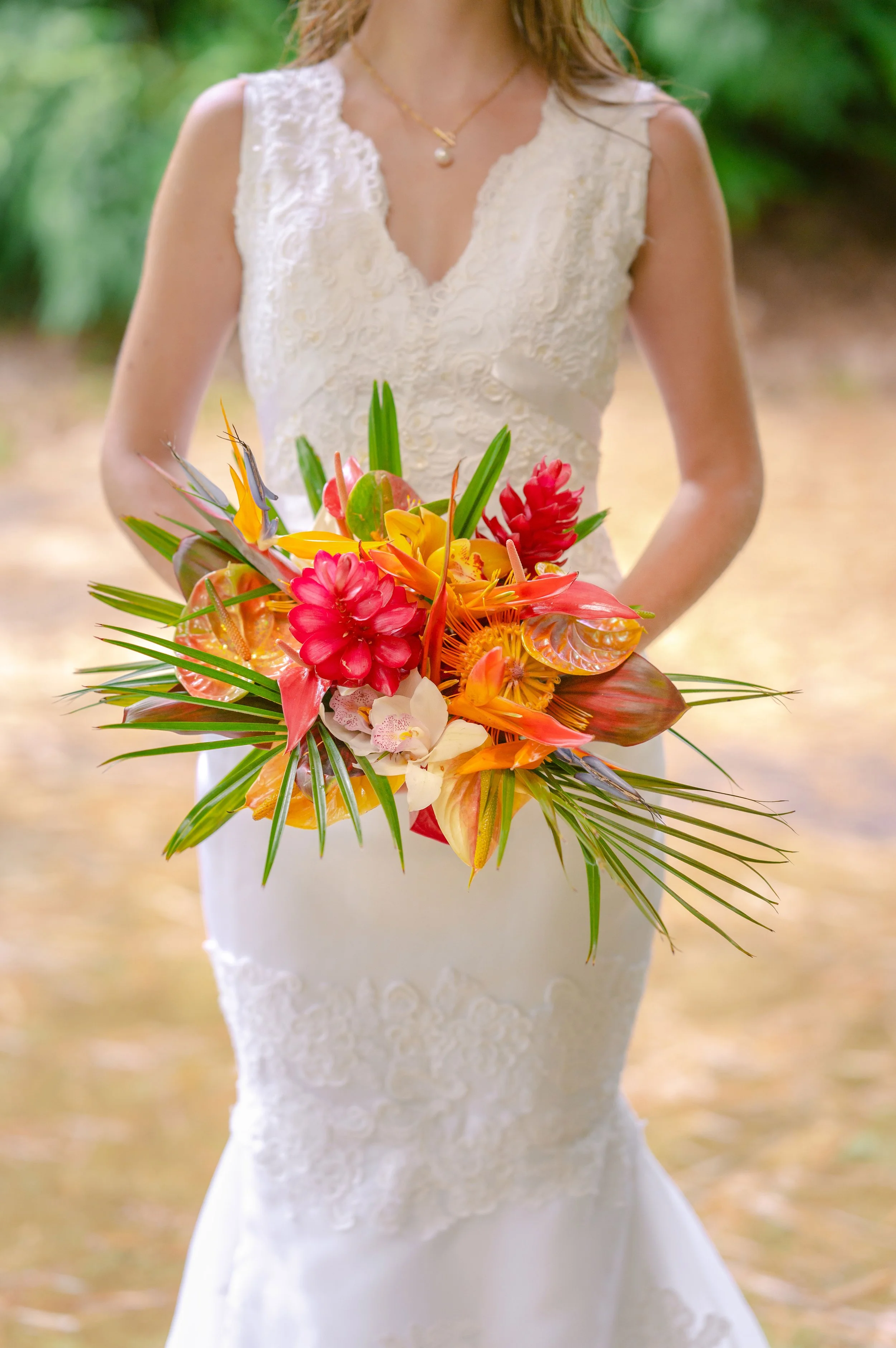 Bride holding a vibrant tropical bouquet with red, yellow, and orange flowers, wearing a white lace wedding dress.