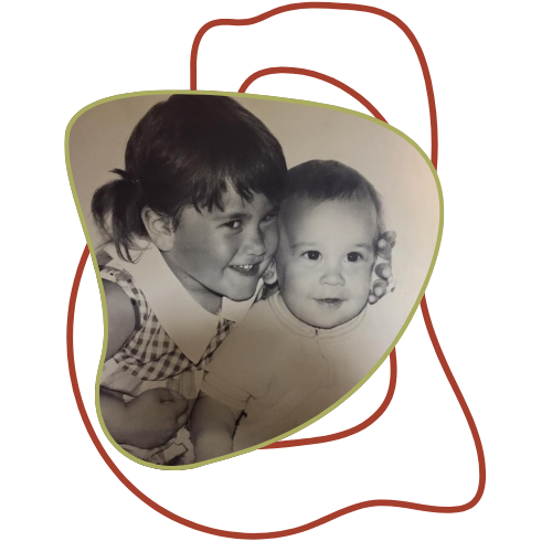 A young girl with dark hair smiling and showing her teeth, holding a young baby with curly hair, in a black and white photo.