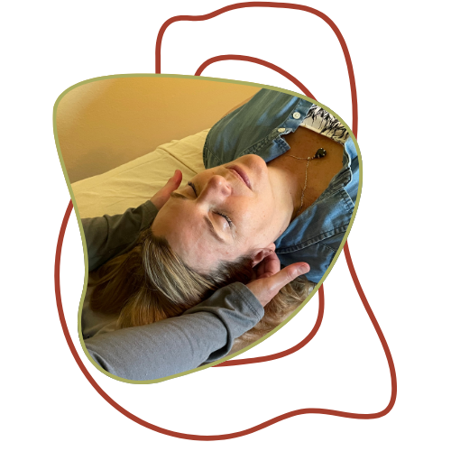 A woman with blonde hair lying on her back with her eyes closed, resting on a pillow, wearing a blue denim shirt and a necklace.