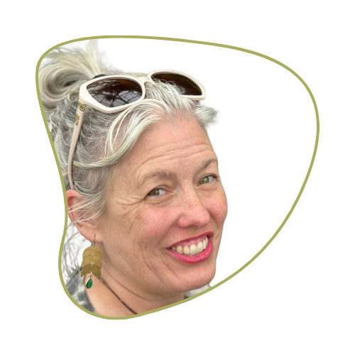 A woman with gray hair tied in a bun, wearing sunglasses on her head and earrings, smiling at the camera.